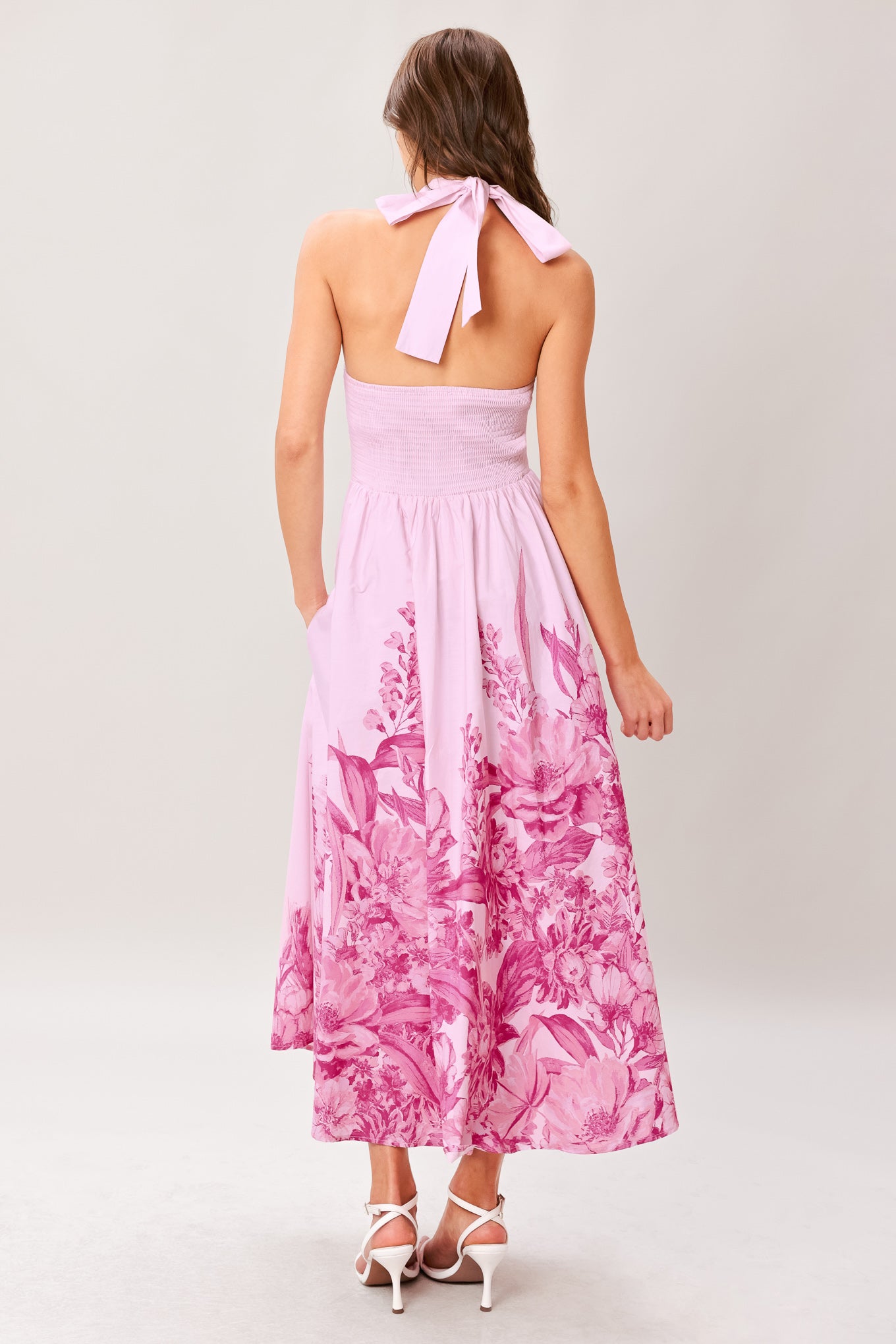 Woman wearing a pink floral printed woven midi dress featuring twist front with back neck tie, full skirt and smocked back bodice