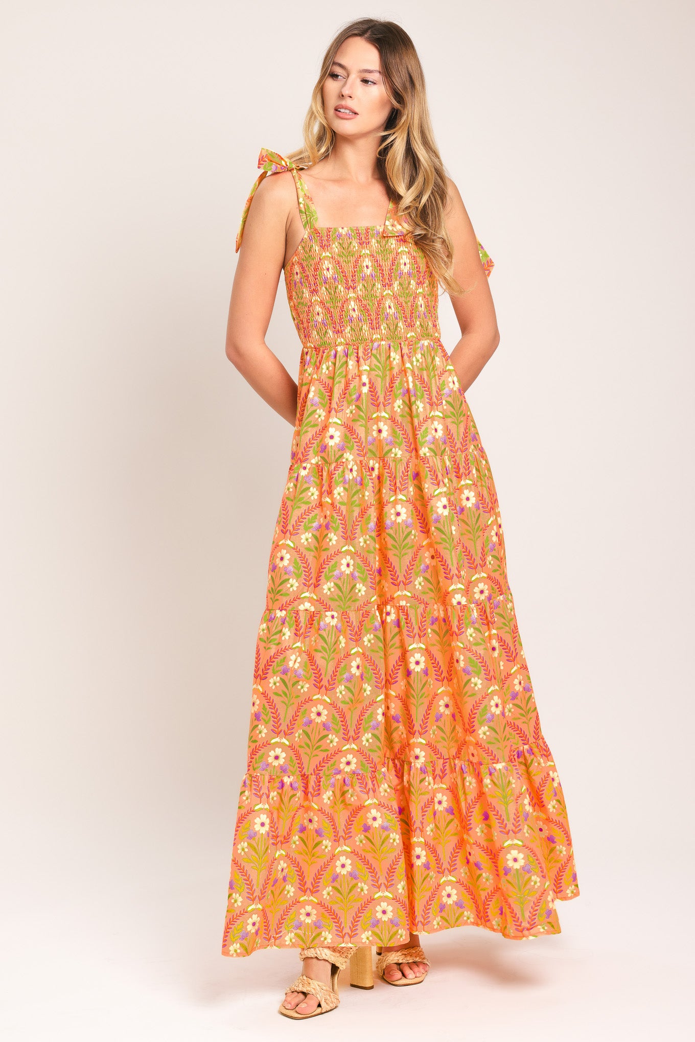 Woman wearing a floral patterned orange maxi dress featuring straight neckline, smocked bodice, shoulder ties and tier skirt | Flying Tomato