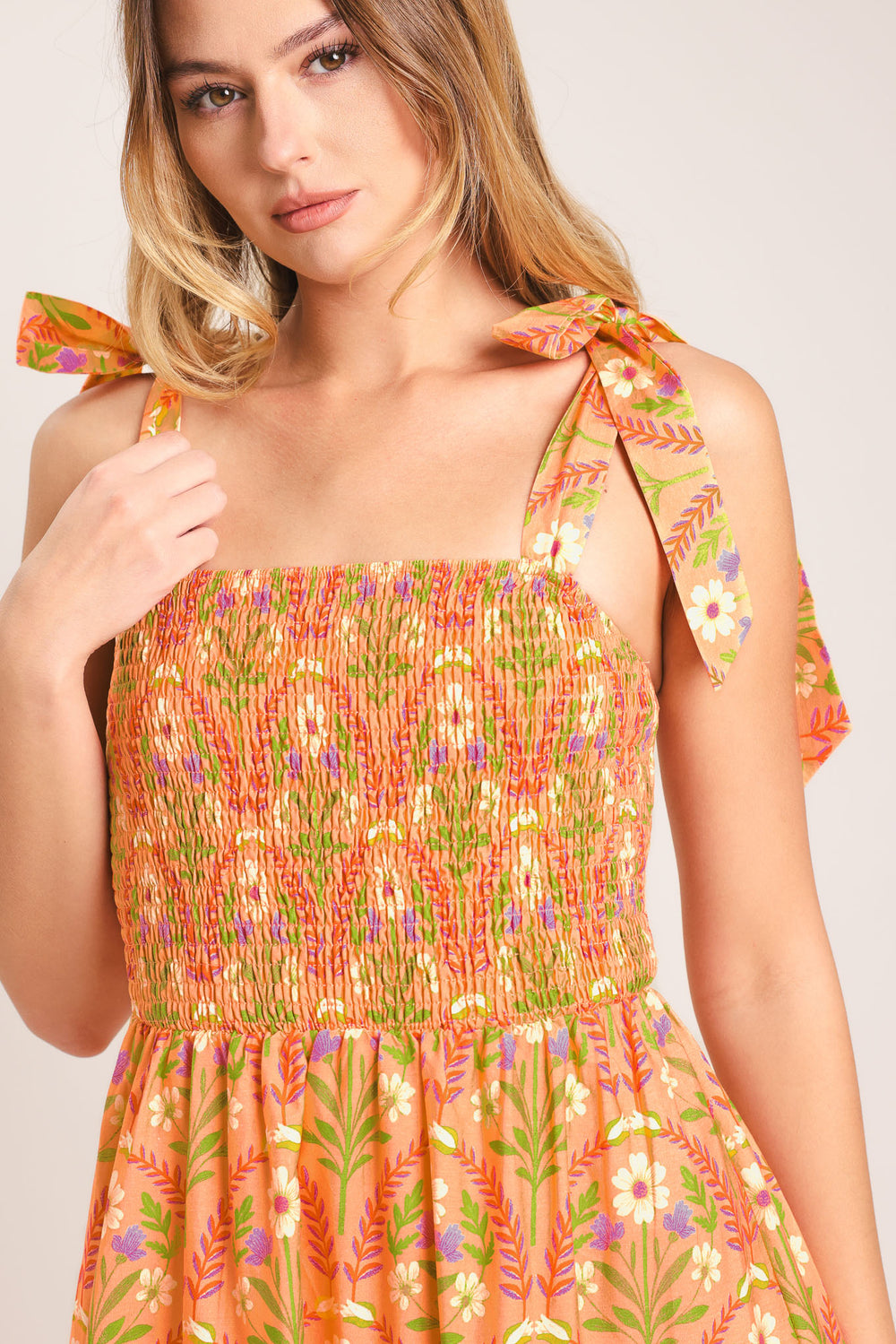 Woman wearing a floral patterned orange maxi dress featuring straight neckline, smocked bodice, shoulder ties and tier skirt | Flying Tomato