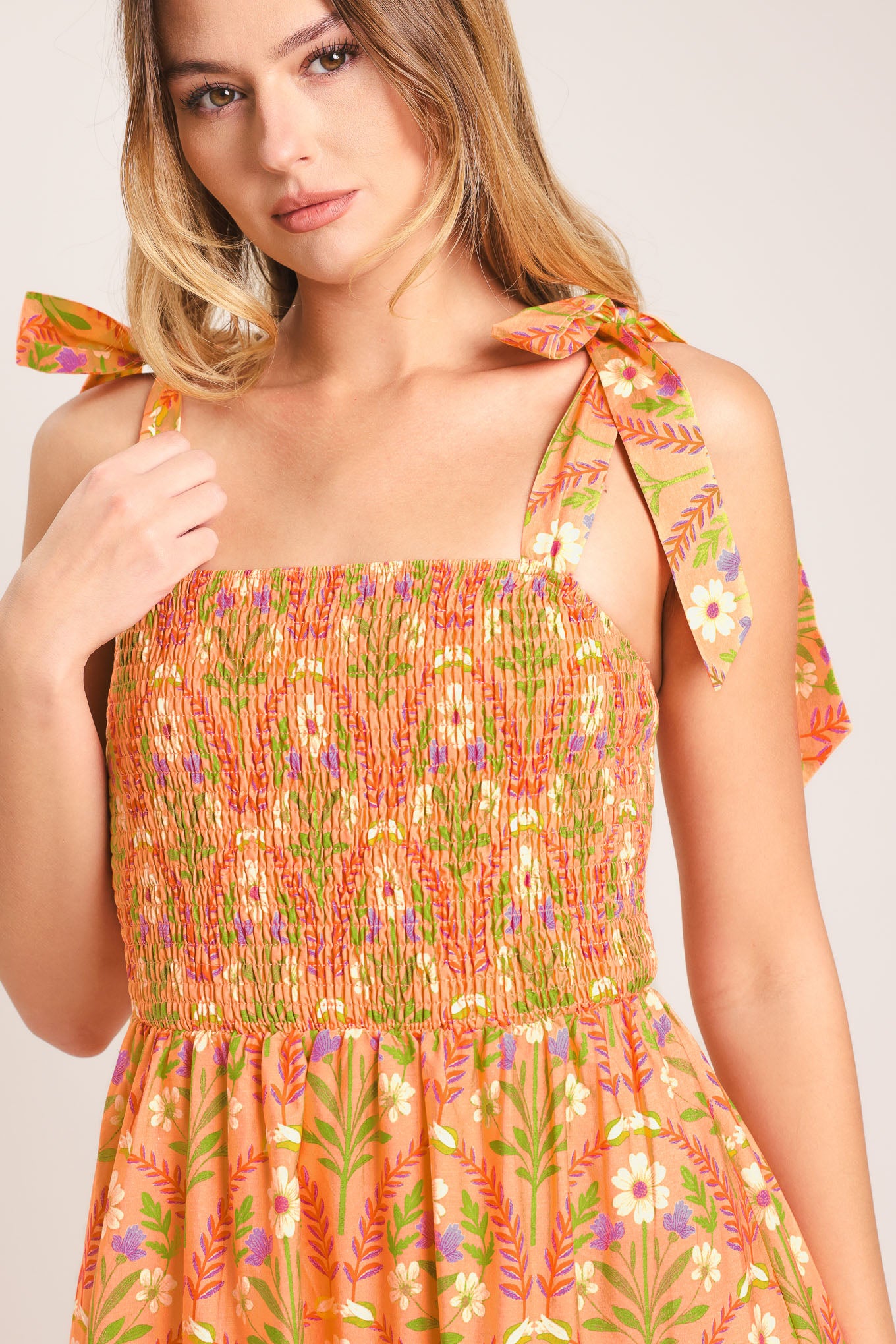 Woman wearing a floral patterned orange maxi dress featuring straight neckline, smocked bodice, shoulder ties and tier skirt | Flying Tomato
