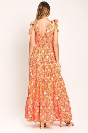 Woman wearing a floral patterned orange maxi dress featuring straight neckline, smocked bodice, shoulder ties and tier skirt | Flying Tomato