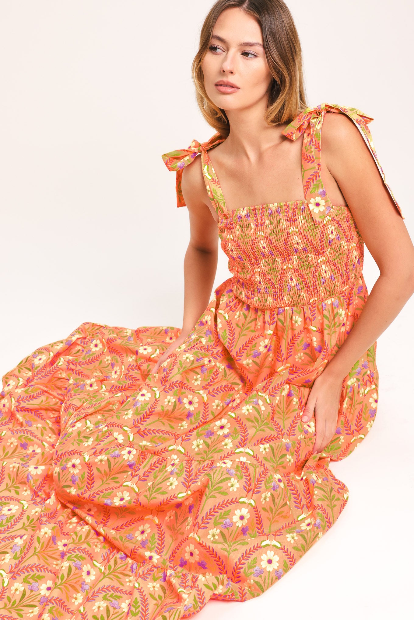 Woman wearing a floral patterned orange maxi dress featuring straight neckline, smocked bodice, shoulder ties and tier skirt | Flying Tomato