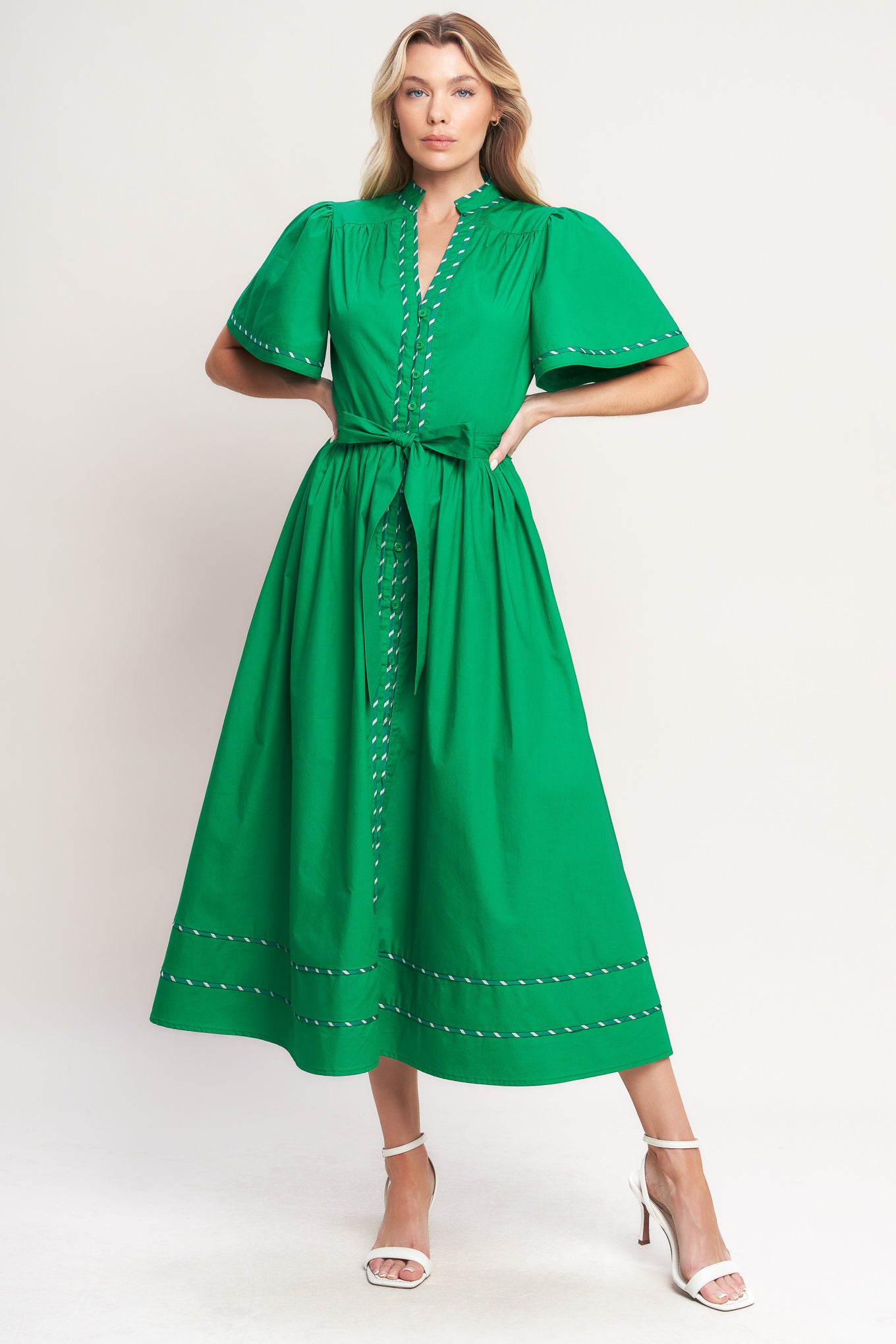 Woman wearing a green midi dress featuring V neckline, short flutter sleeve, button down, self sash tie, contrasting binding and full skirt | Flying Tomato