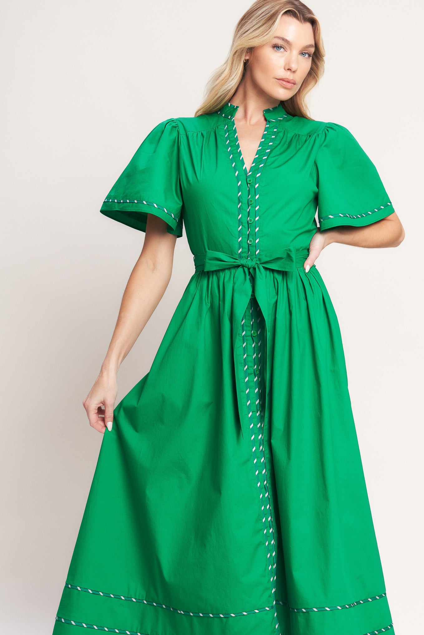 Woman wearing a green midi dress featuring V neckline, short flutter sleeve, button down, self sash tie, contrasting binding and full skirt | Flying Tomato
