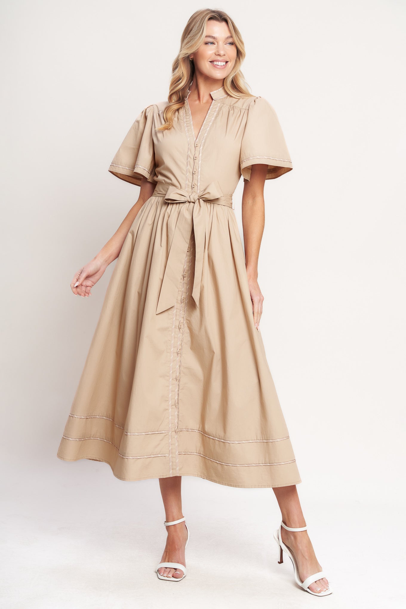 Woman wearing a taupe midi dress featuring V neckline, short flutter sleeve, button down, self sash tie, contrasting binding and full skirt | Flying Tomato