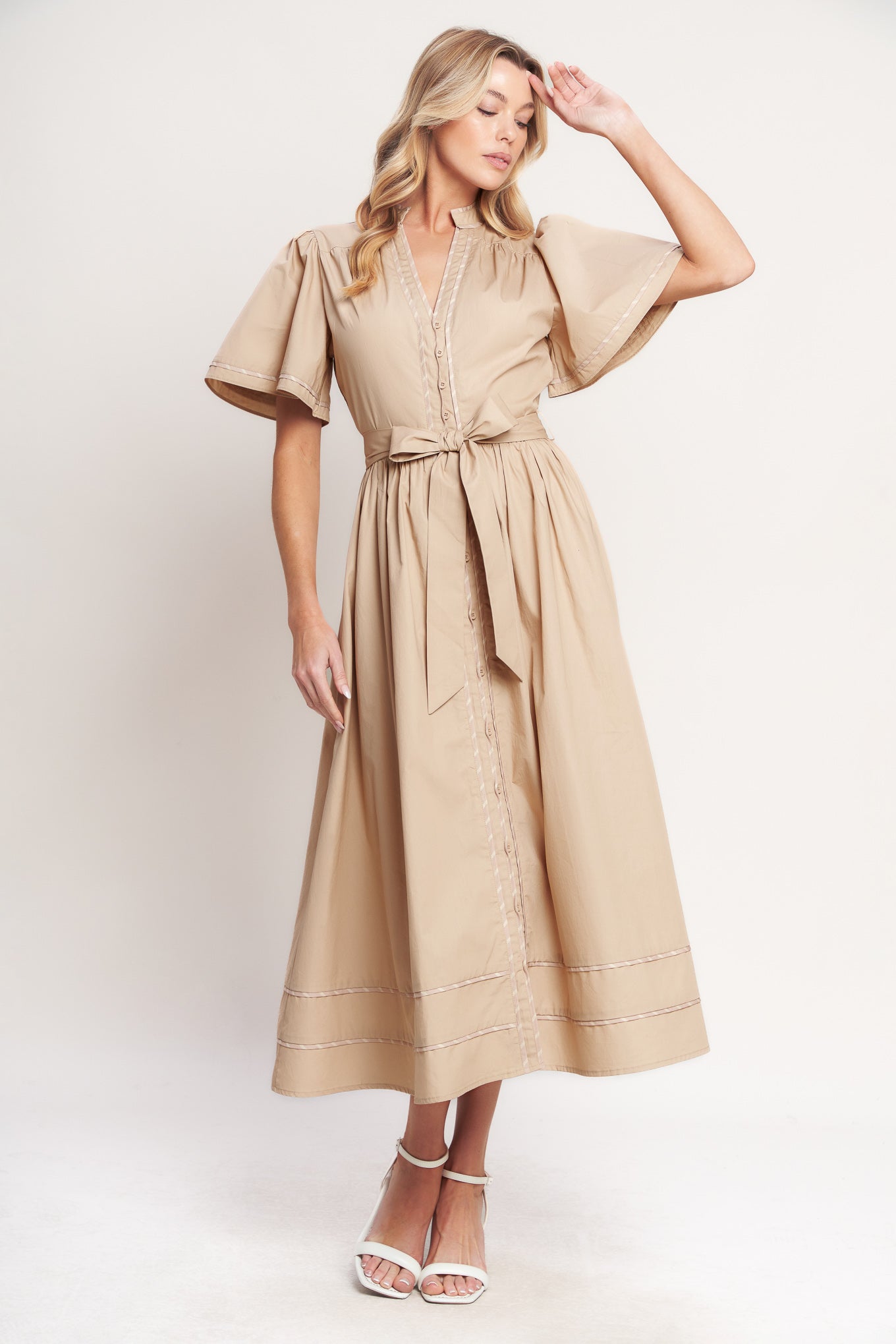 Woman wearing a beige midi dress featuring V neckline, short flutter sleeve, button down, self sash tie, contrasting binding and full skirt | Flying Tomato