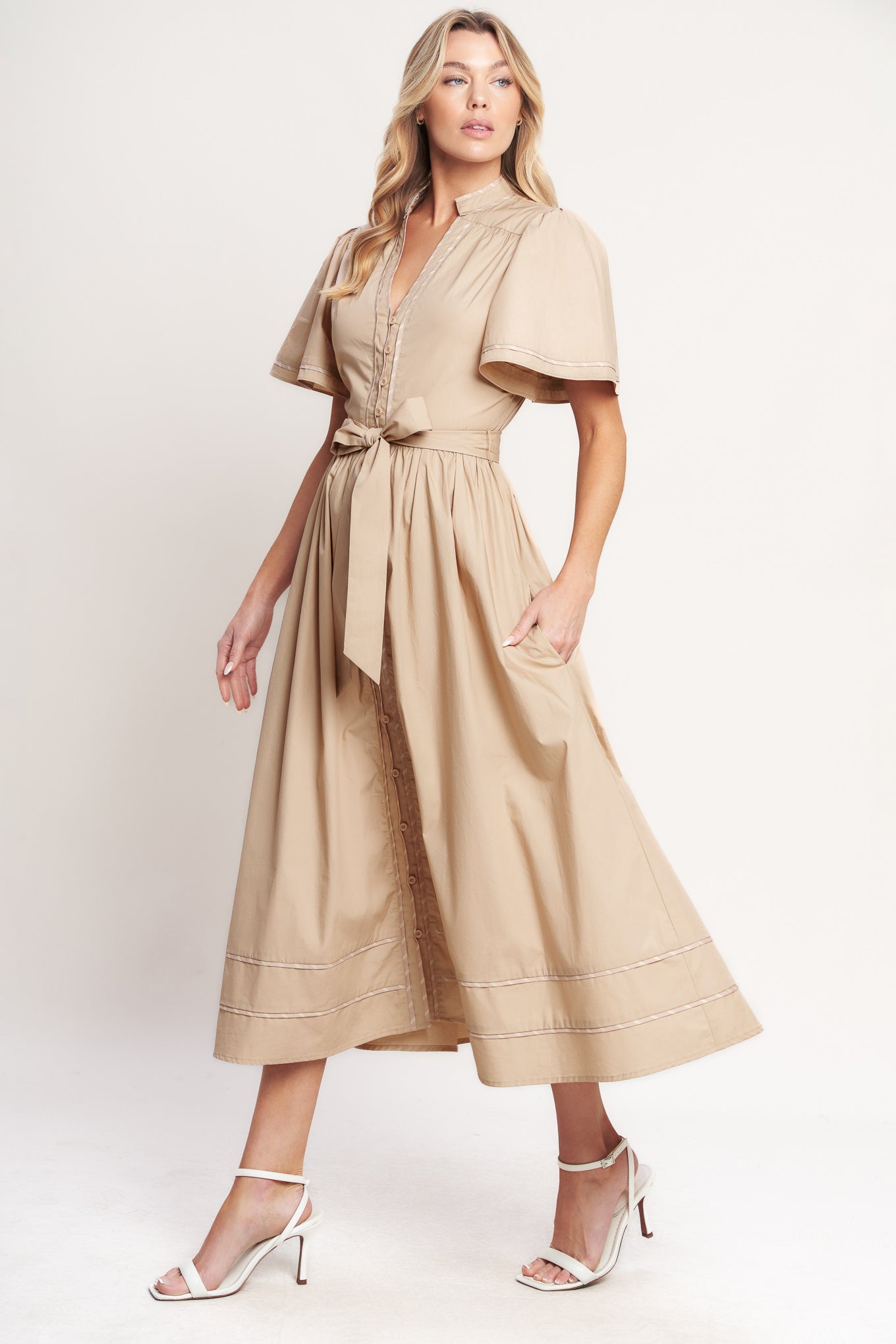Woman wearing a beige midi dress featuring V neckline, short flutter sleeve, button down, self sash tie, contrasting binding and full skirt | Flying Tomato