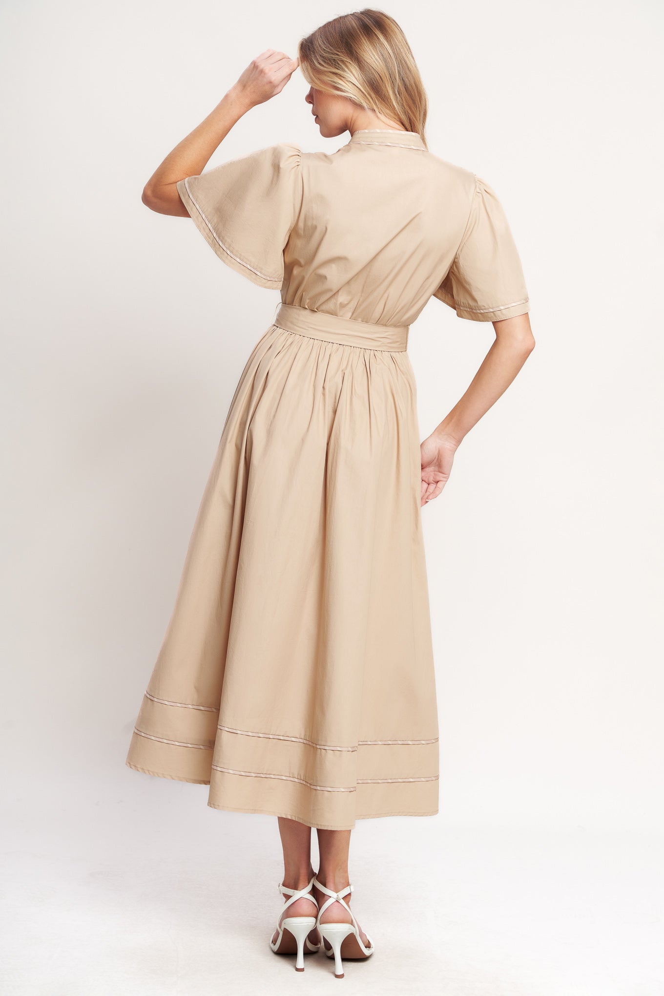 Woman wearing a beige midi dress featuring V neckline, short flutter sleeve, button down, self sash tie, contrasting binding and full skirt | Flying Tomato