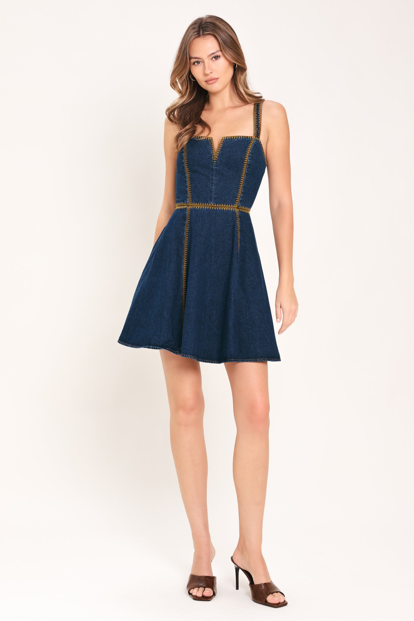Woman wearing a blue denim mini dress with embroidered detail featuring straight neckline with V cut out, straps, circle skirt, and back zipper closure | Flying Tomato