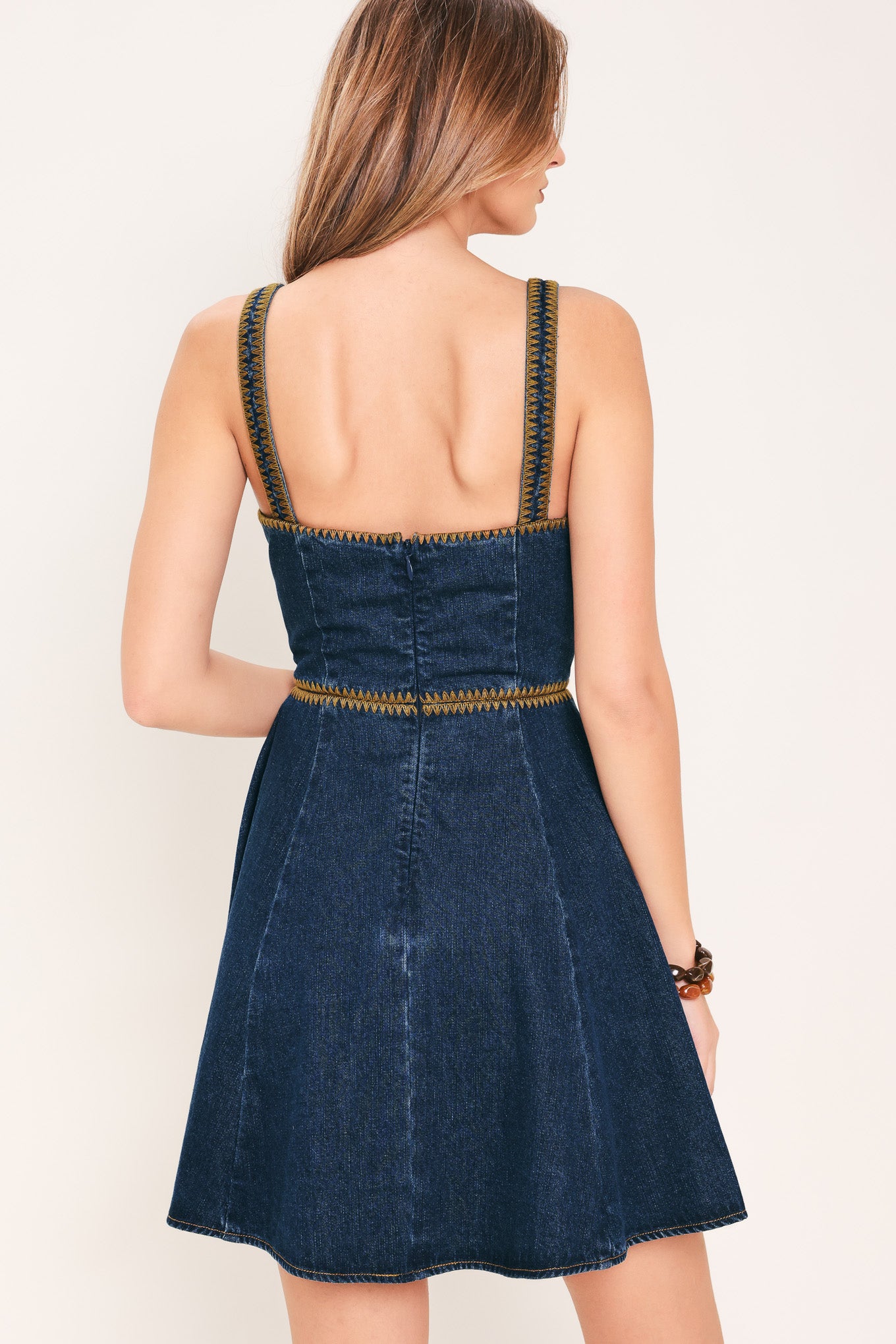 Woman wearing a blue denim mini dress with embroidered detail featuring straight neckline with V cut out, straps, circle skirt, and back zipper closure | Flying Tomato