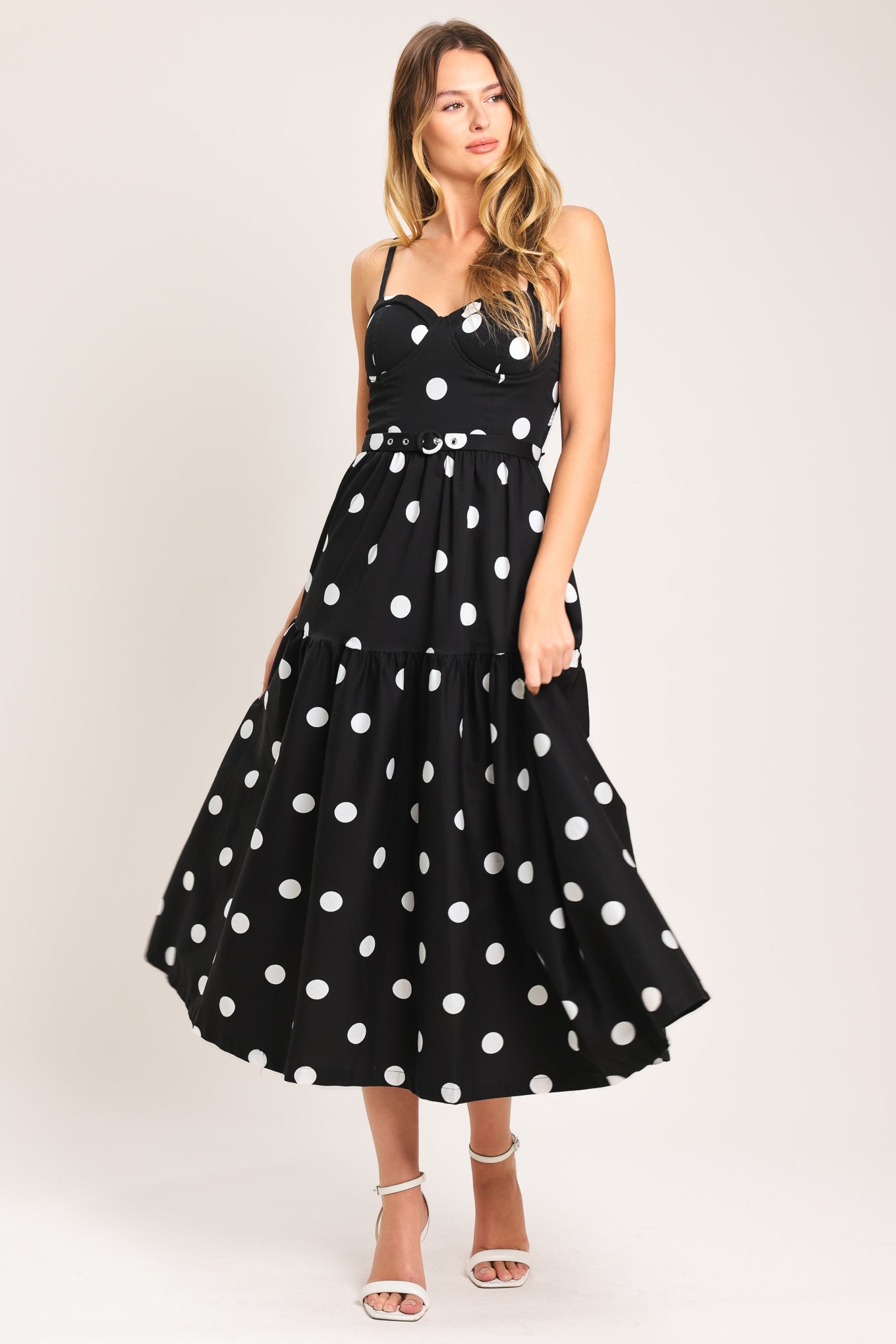 Woman wearing a black midi dress with white polka dots featuring bustier bodice, self belt, full skirt with single tier and smocked back bodice | Flying Tomato