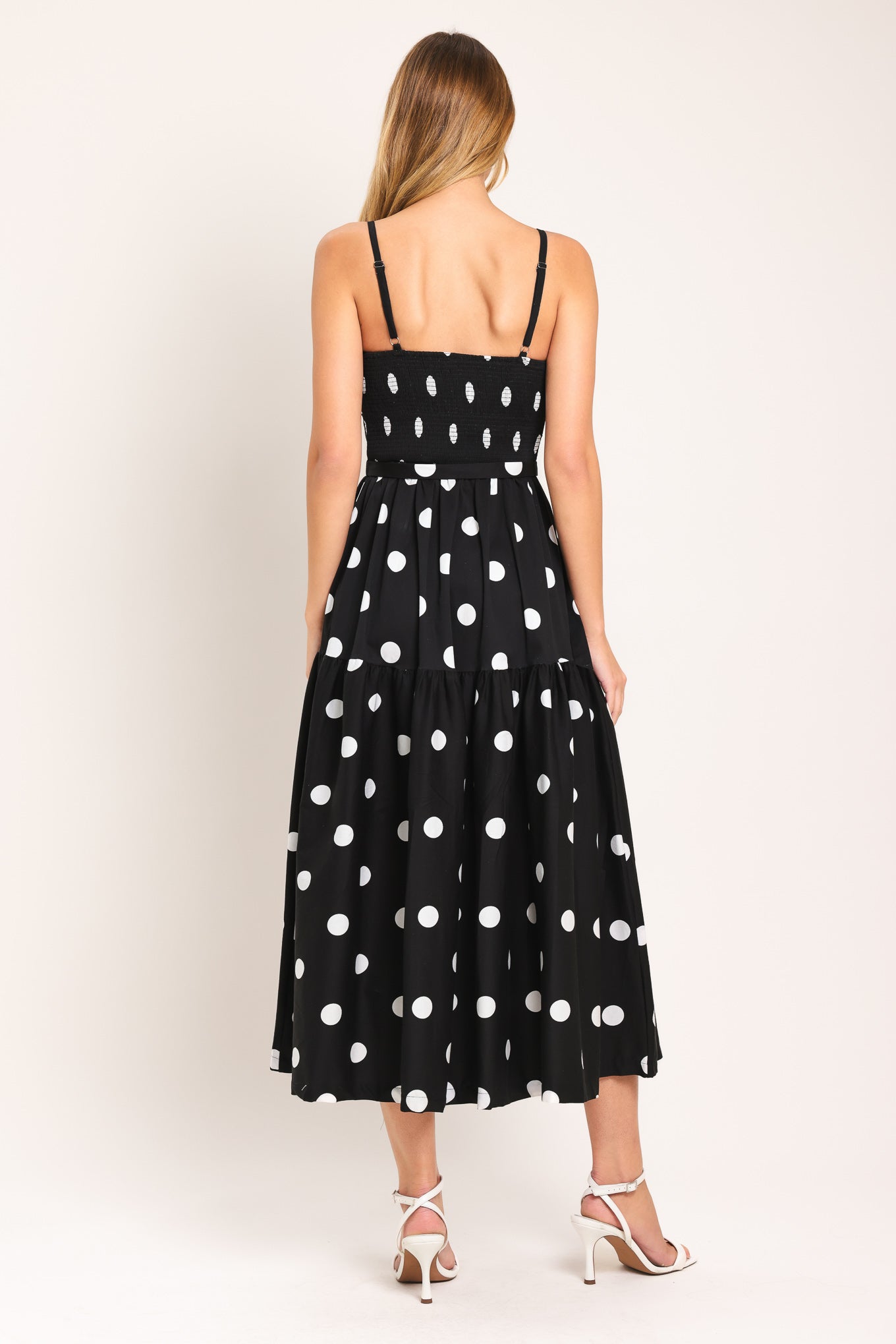 Woman wearing a black midi dress with white polka dots featuring bustier bodice, self belt, full skirt with single tier and smocked back bodice | Flying Tomato
