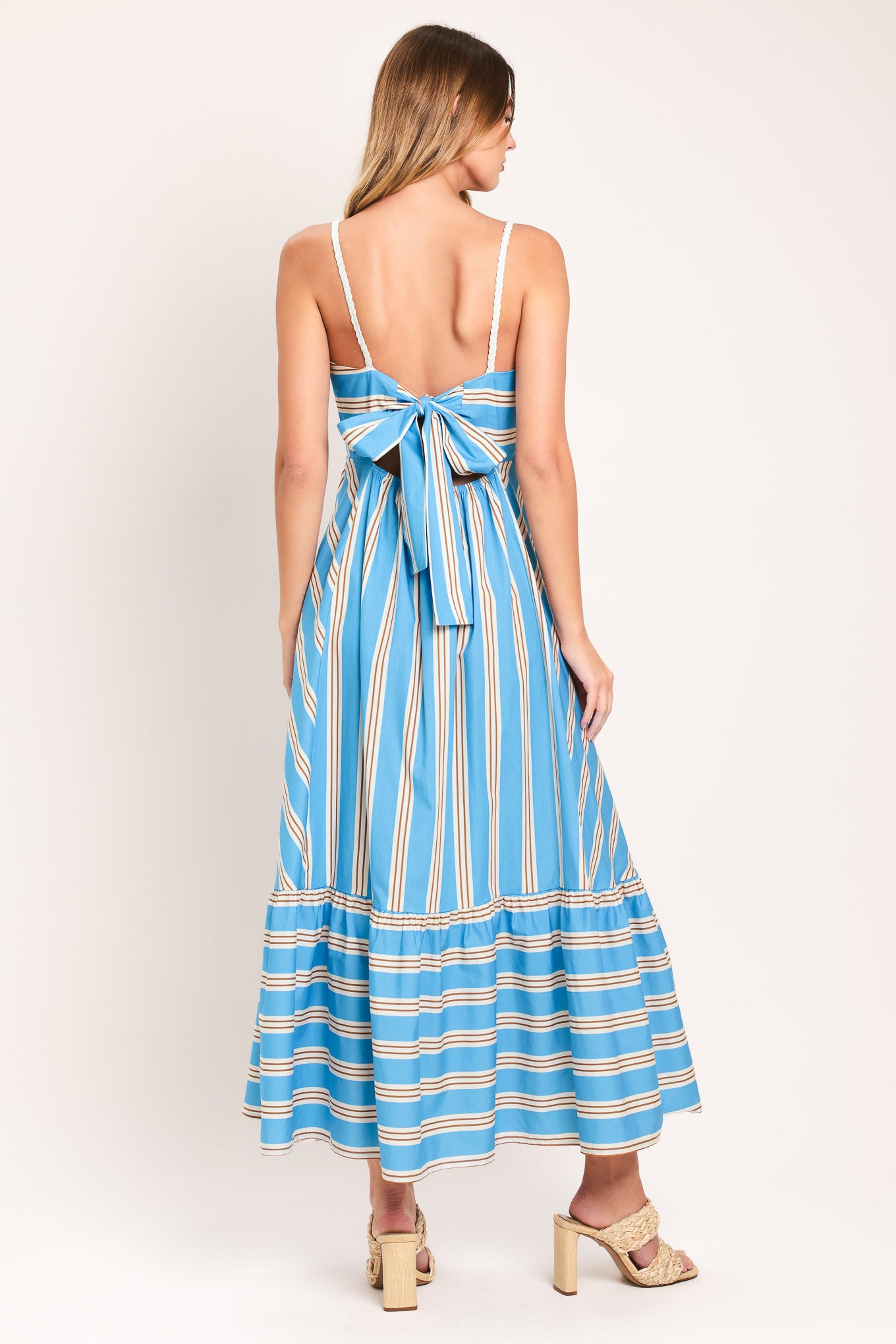 Woman wearing a blue and white striped midi dress featuring straight neckline, braided strap, circle skirt, ruffle hem, bare back with tie closure | Flying Tomato