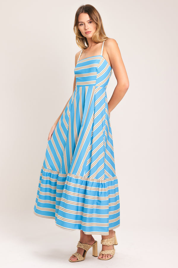 Woman wearing a blue and white striped midi dress featuring straight neckline, braided strap, circle skirt, ruffle hem, bare back with tie closure | Flying Tomato
