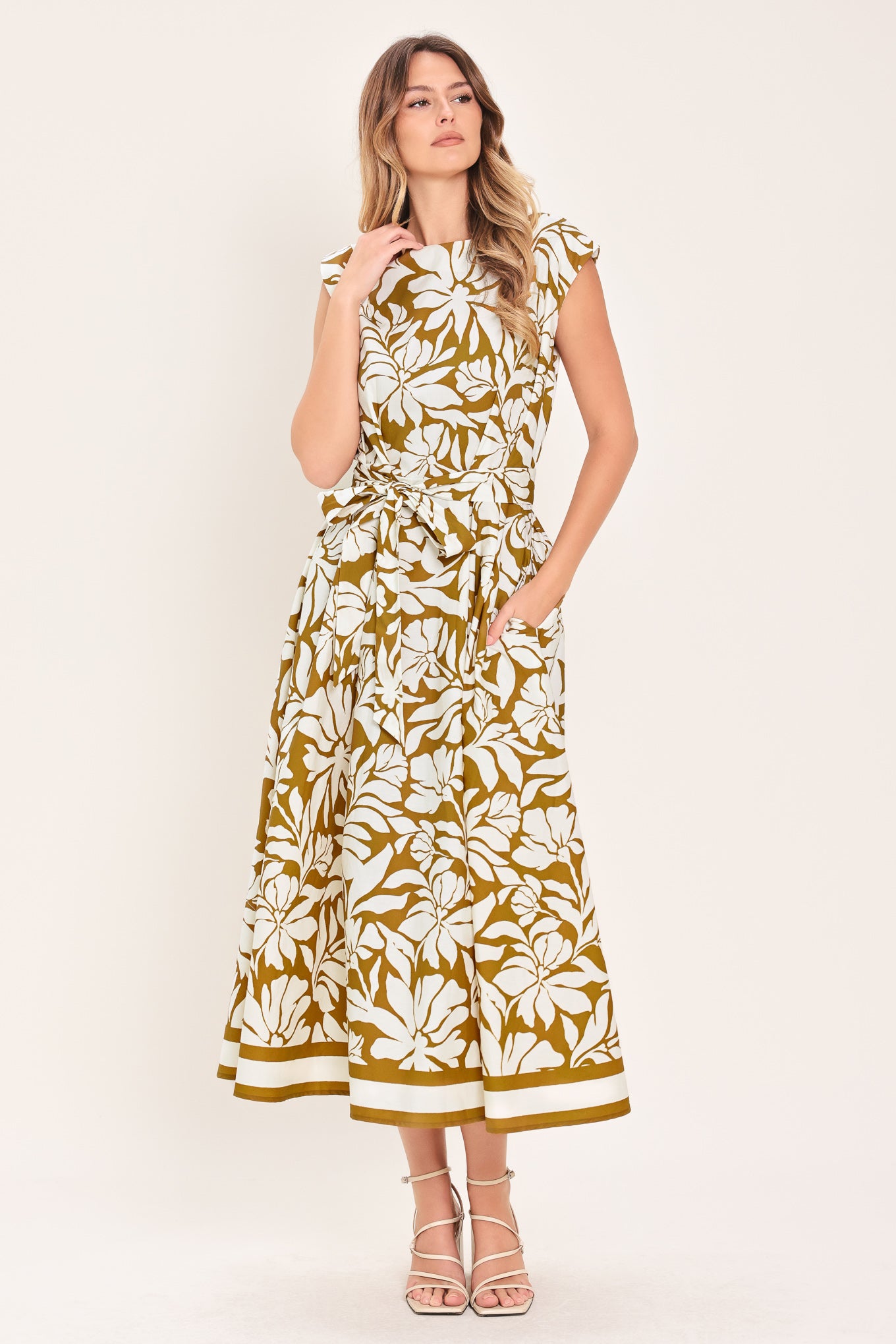 Woman wearing a camel and white short sleeve midi dress with round neckline, self sash and back neck button closure with a tropical floral pattern | Flying Tomato