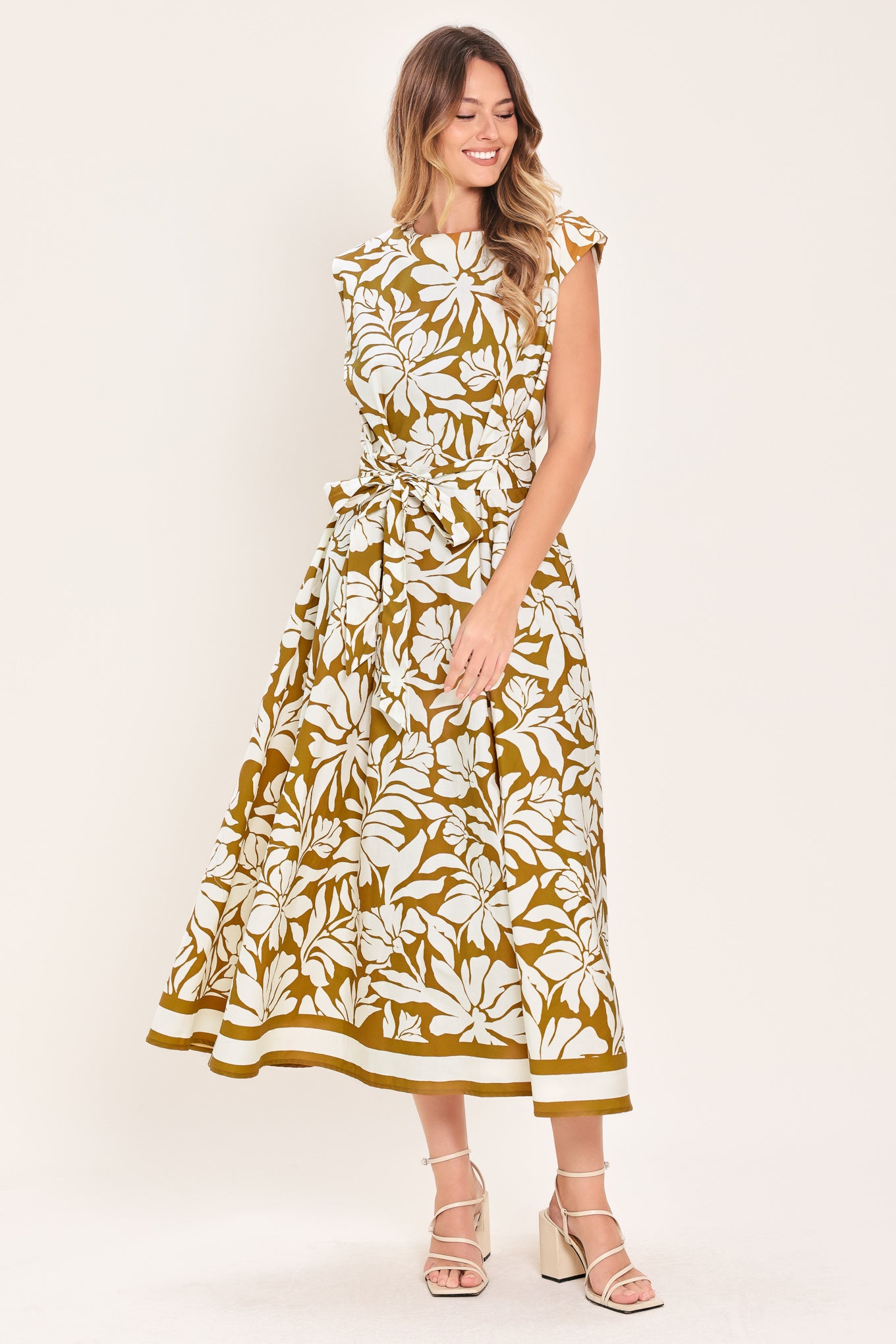 Woman wearing a camel and white short sleeve midi dress with round neckline, self sash and back neck button closure with a tropical floral pattern | Flying Tomato