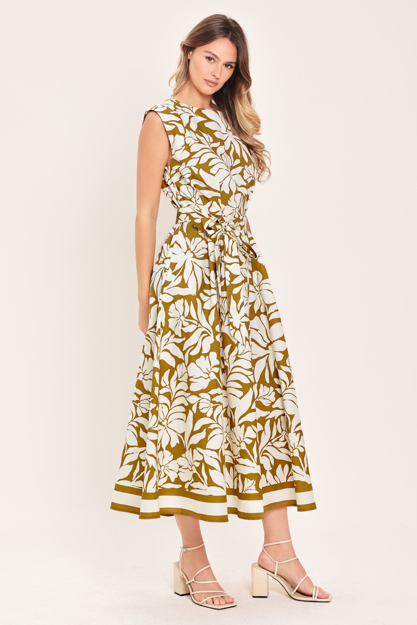 Woman wearing a camel and white short sleeve midi dress with round neckline, self sash and back neck button closure with a tropical floral pattern | Flying Tomato