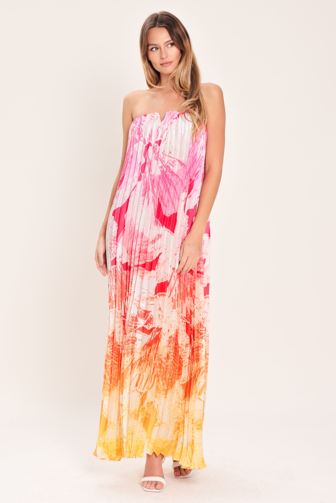 Woman wearing a pink with orange and yellow ombre pleated maxi dress with front V, strapless and back zipper closure | Flying Tomato