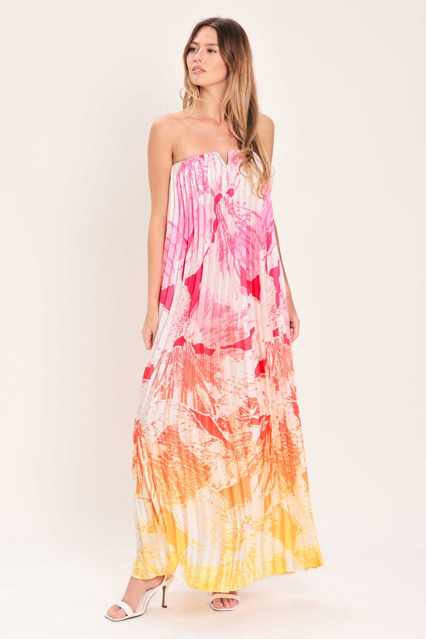 Woman wearing a pink with orange and yellow ombre pleated maxi dress with front V, strapless and back zipper closure | Flying Tomato
