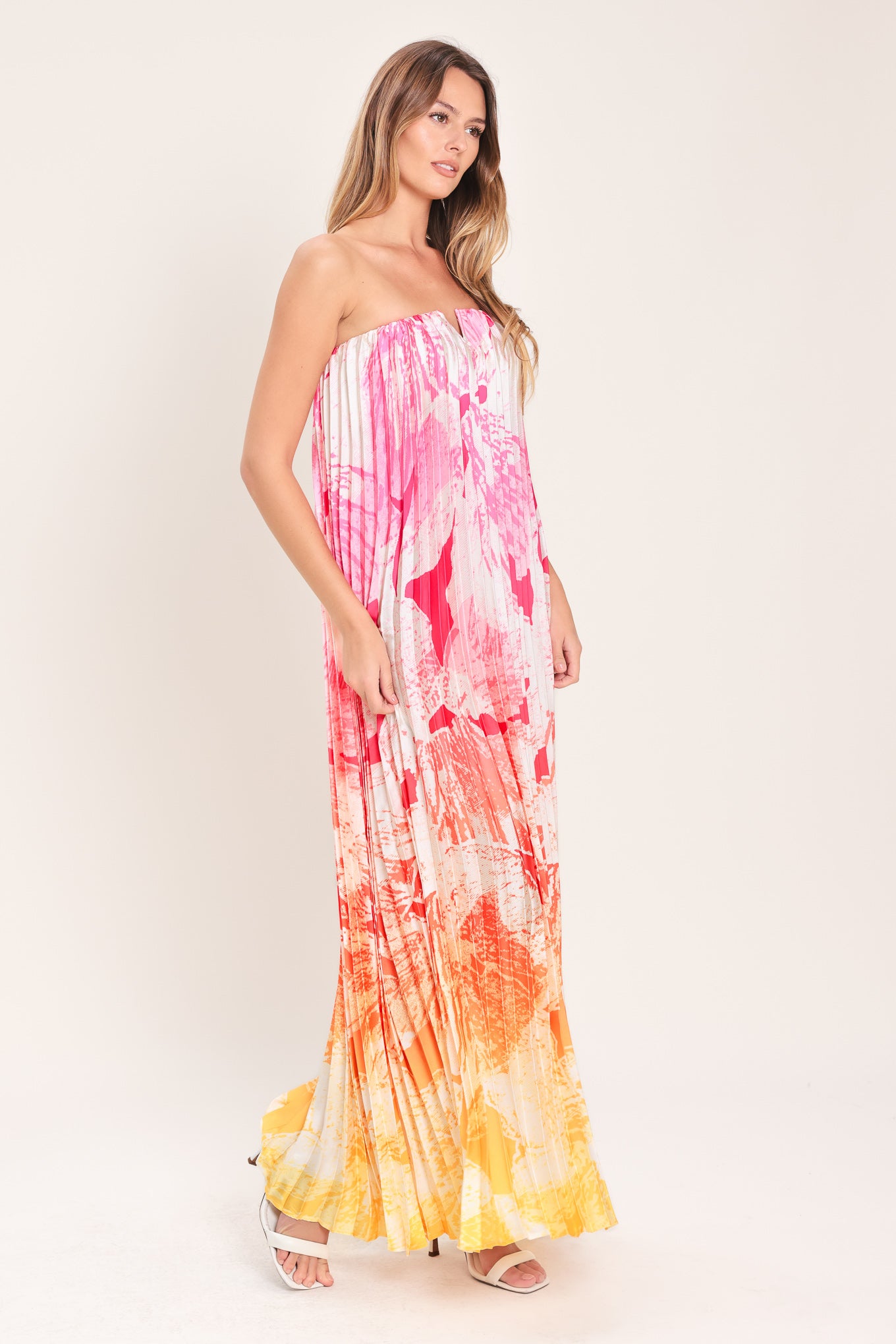 Woman wearing a pink with orange and yellow ombre pleated maxi dress with front V, strapless and back zipper closure | Flying Tomato