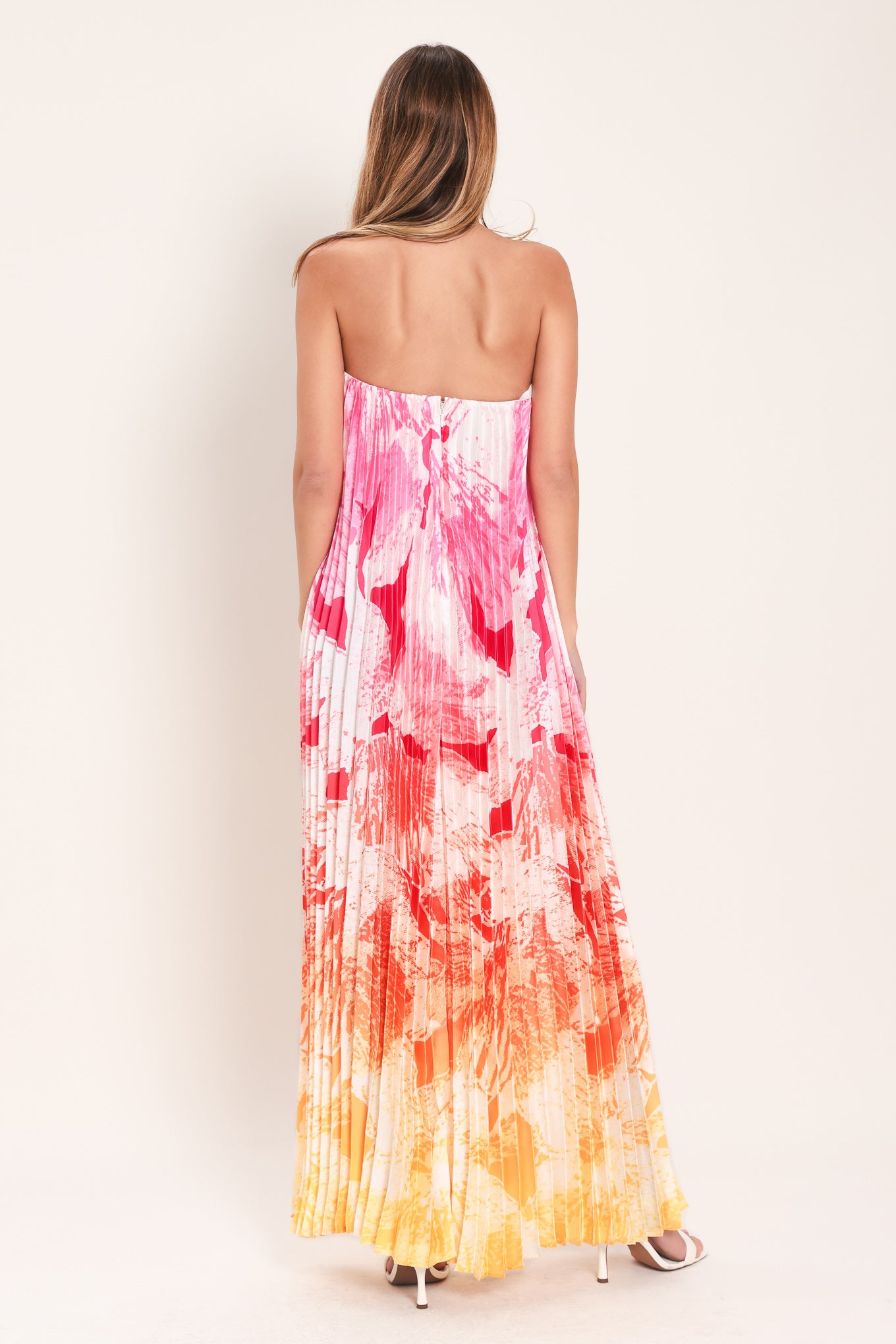 Woman wearing a pink with orange and yellow ombre pleated maxi dress with front V, strapless and back zipper closure | Flying Tomato