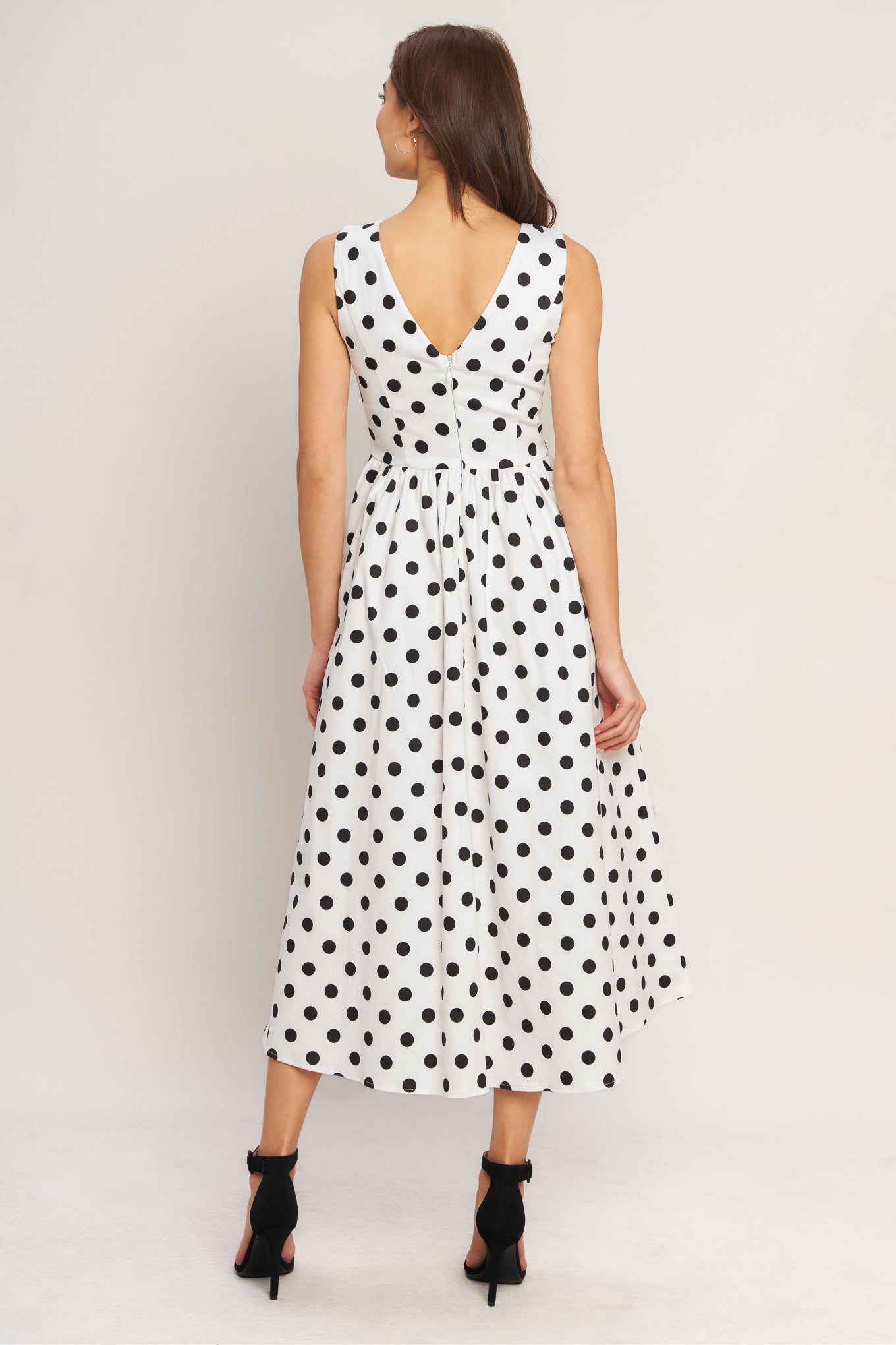 Woman wearing a black and white polka dot dress on a plain background