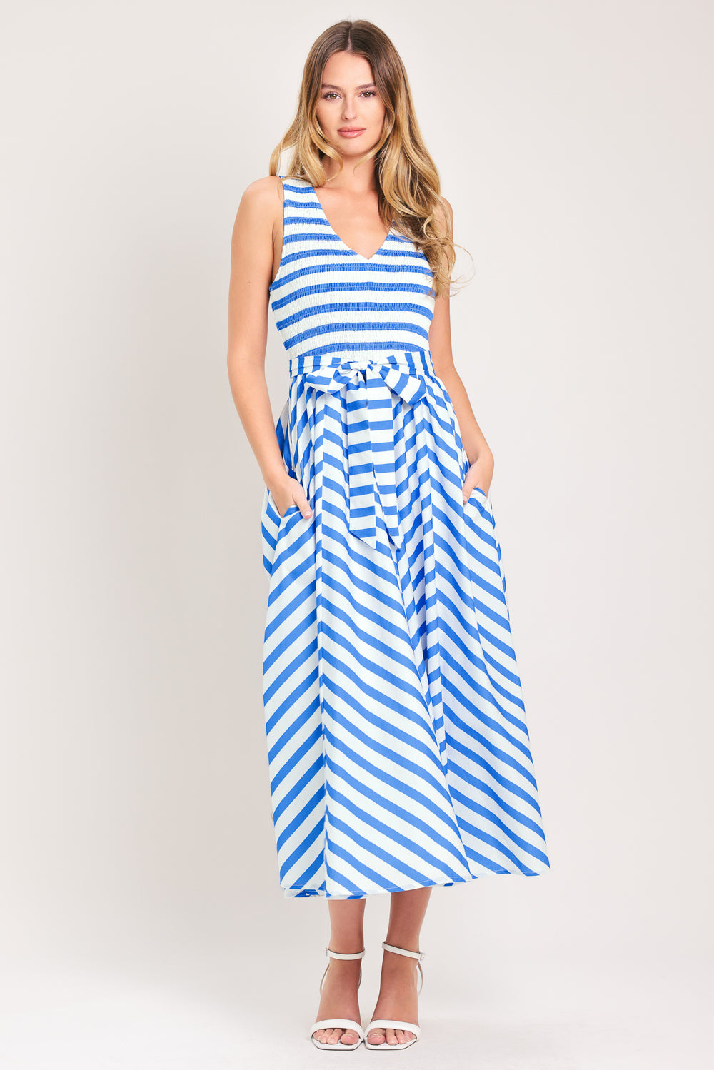 Woman wearing a blue and white striped  midi dress featuring V neckline, sleeveless, smocked bodice, self sash tie and full skirt | Flying Tomato