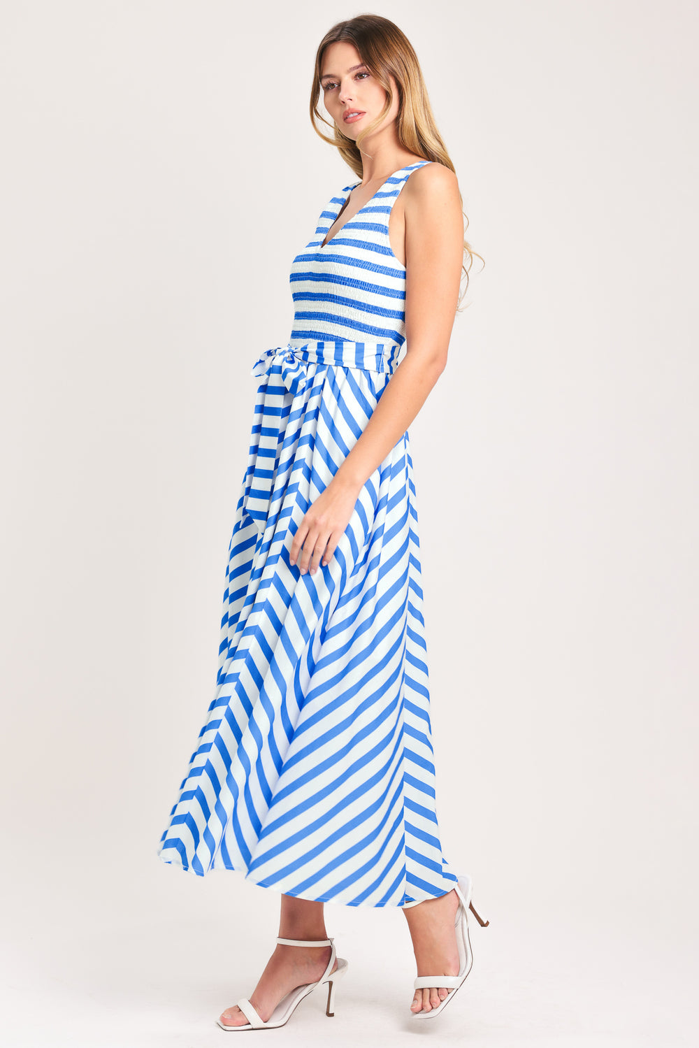 Woman wearing a blue and white striped  midi dress featuring V neckline, sleeveless, smocked bodice, self sash tie and full skirt | Flying Tomato