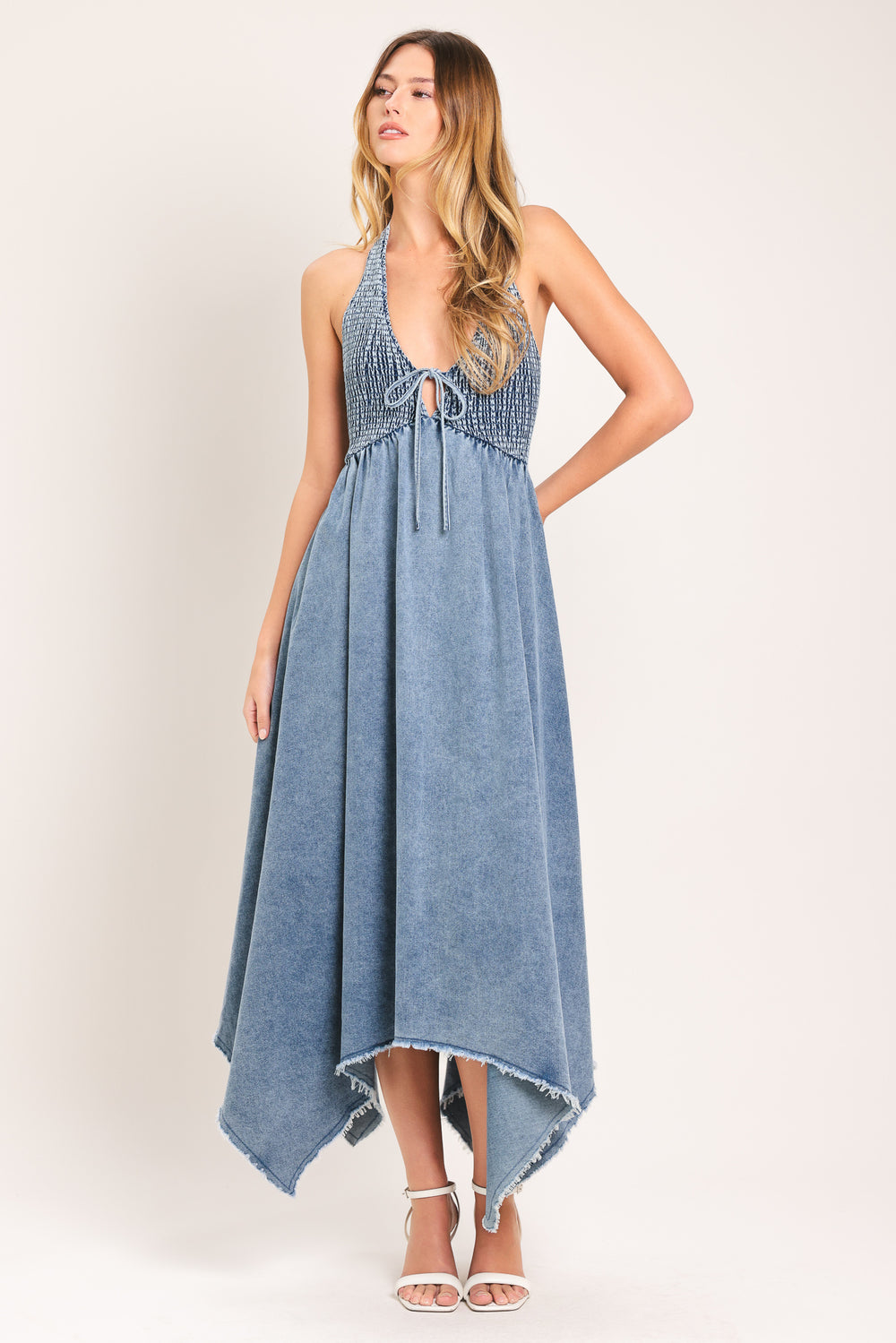 Woman wearing a blue denim midi dress featuring smocked halter bodice with front tie, fray hem and back neck tie | Flying Tomato