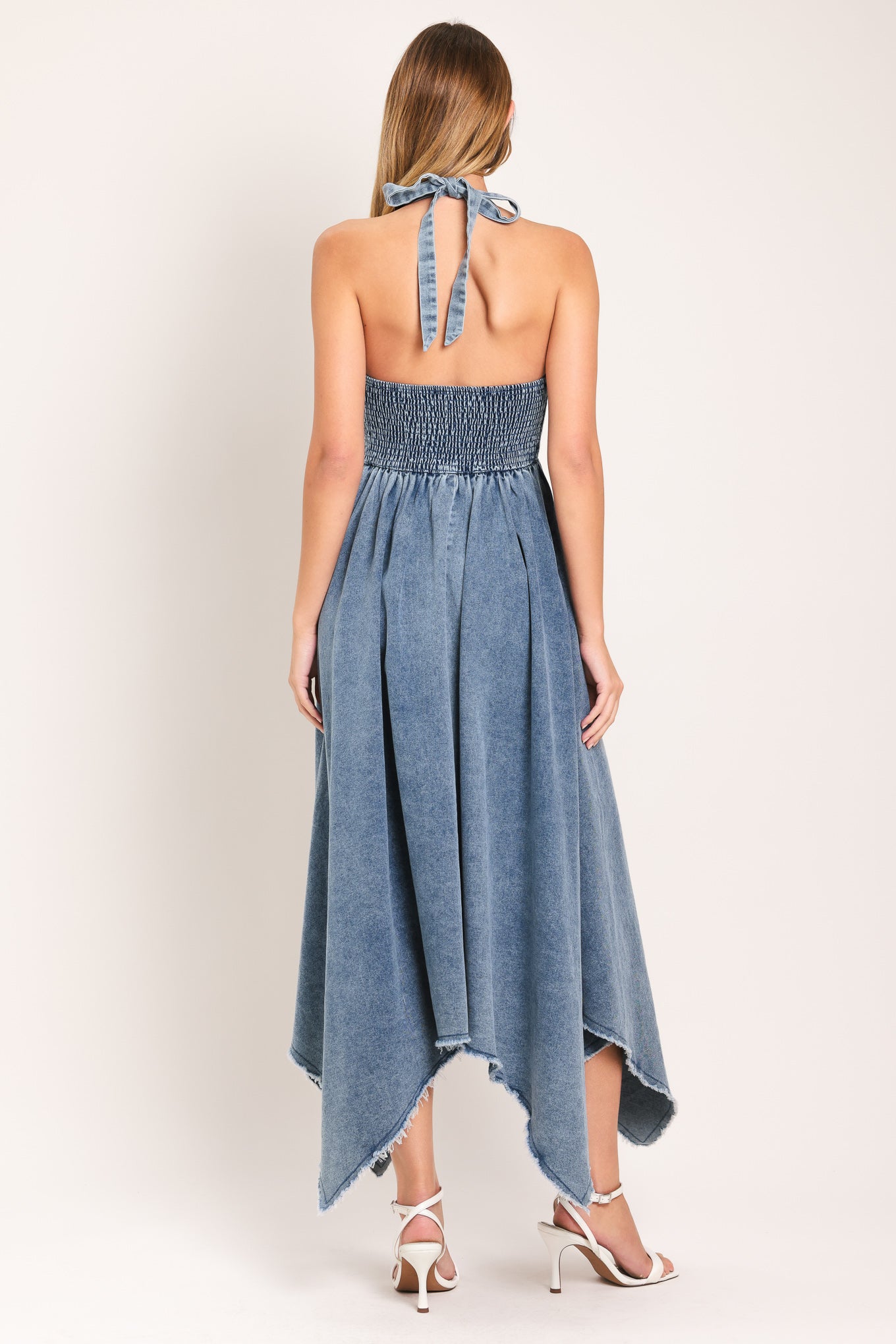 Woman wearing a blue denim midi dress featuring smocked halter bodice with front tie, fray hem and back neck tie | Flying Tomato