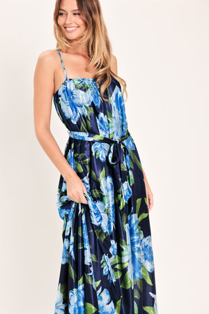 Woman wearing a navy blue with lighter blue flowers printed maxi dress with straight neckline, straps and self sash tie | Flying Tomato