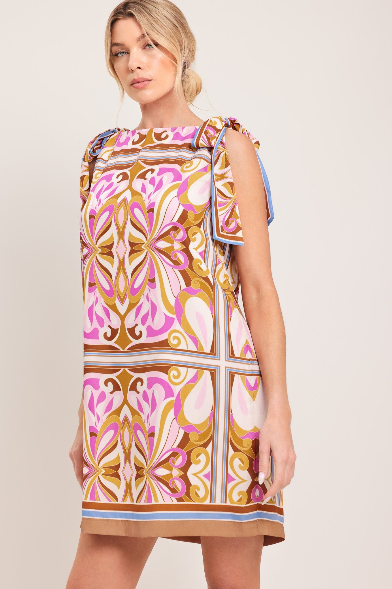 Woman wearing a sleeveless retro patterned mini dress featuring a wide neckline, shoulder ties, and back neck button closure | Flying Tomato