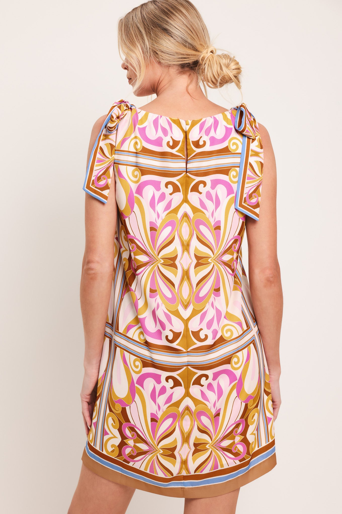 Woman wearing a sleeveless retro patterned mini dress featuring a wide neckline, shoulder ties, and back neck button closure | Flying Tomato
