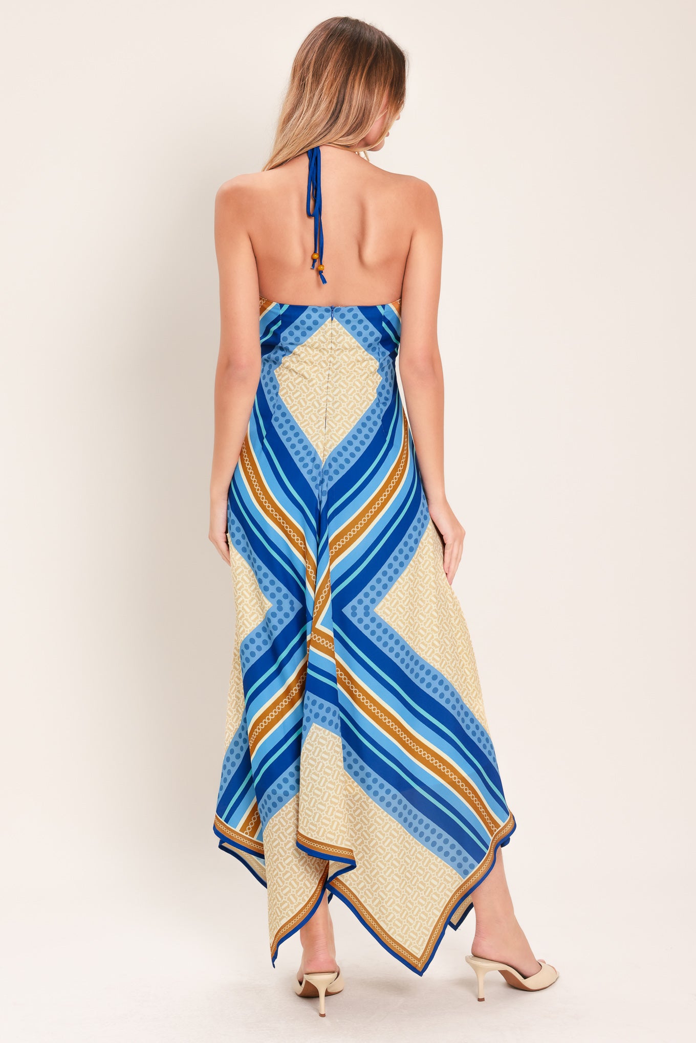 Woman wearing a blue and gold midi dress featuring halter neckline with tie, hanky hem and back zipper closure | Flying Tomato