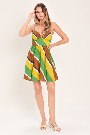 Woman wearing a green, brown, and yellow mini dress with straps, waist yoke, full skirt and smocked back bodice | Flying Tomato