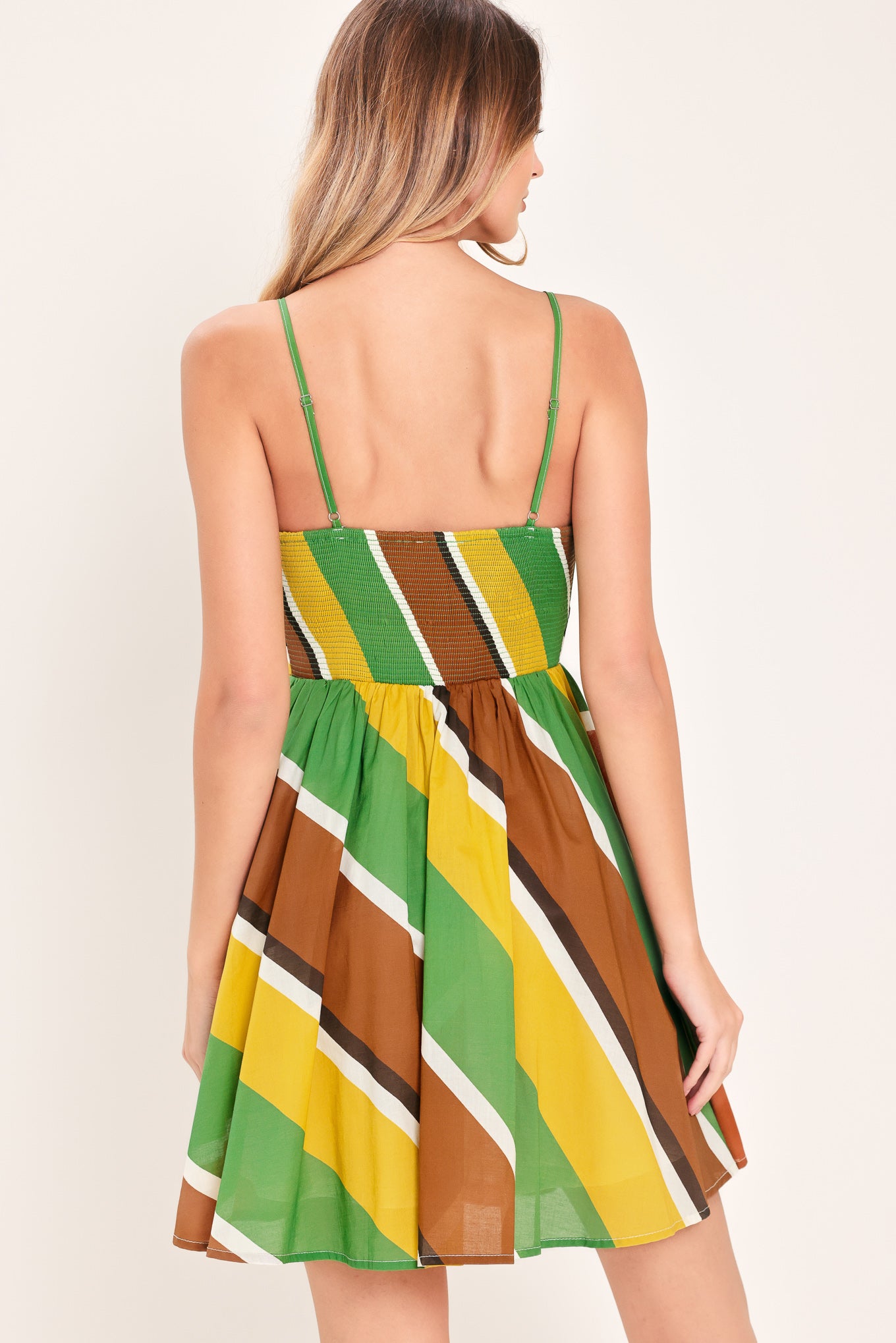 Woman wearing a green, brown, and yellow mini dress with straps, waist yoke, full skirt and smocked back bodice | Flying Tomato