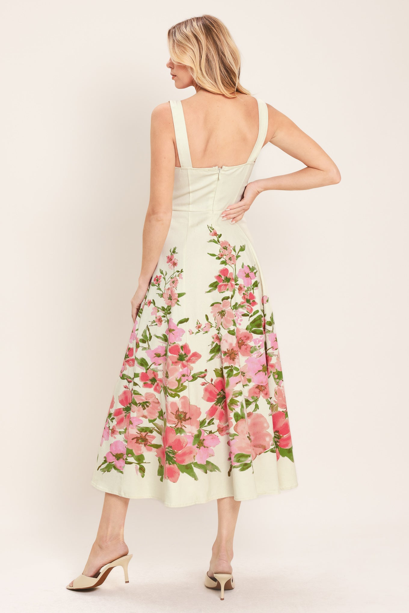 Woman wearing an ivory midi dress with pink floral pattern featuring sweetheart neckline, straps, button down detail, circle skirt and back zipper closure | Flying Tomato