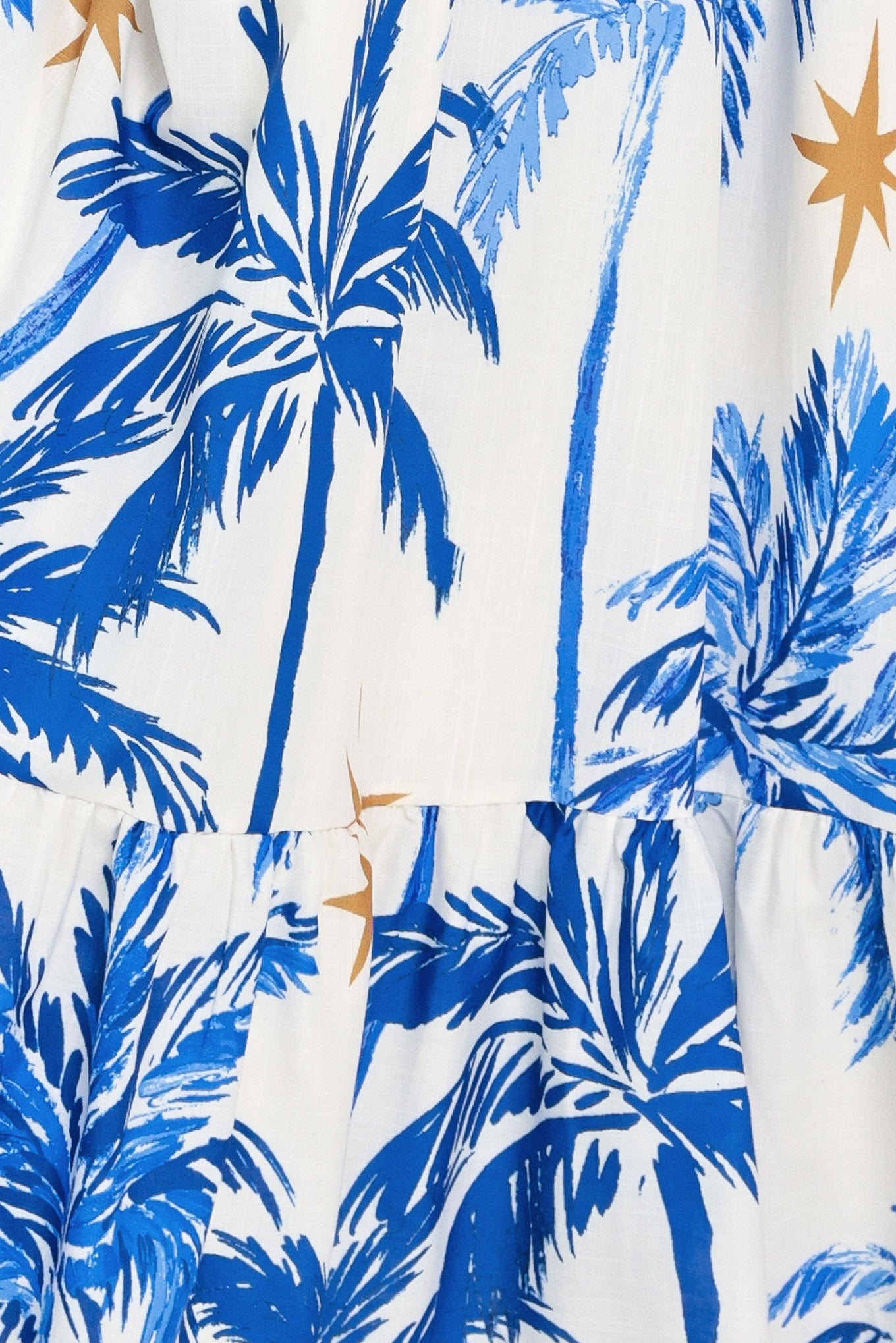 Close up of a blue and white palm tree patterned maxi dress featuring smocked bodice, shoulder straps, full skirt with ruffle hem | Flying Tomato