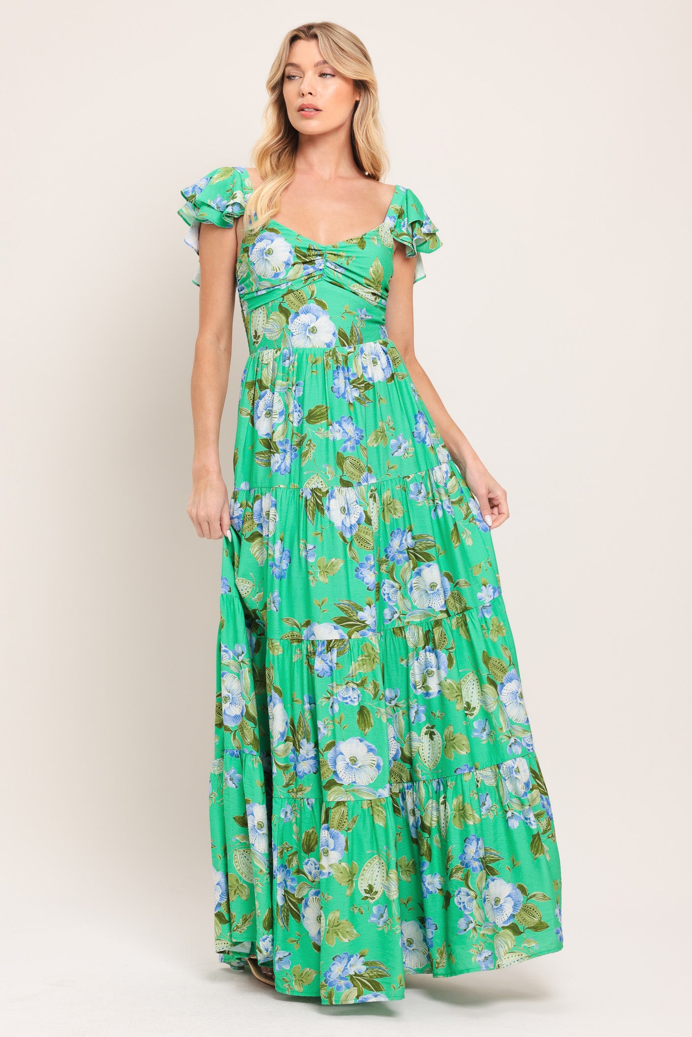 Woman wearing a green and blue floral maxi dress featuring sweetheart neckline, shirred bust, double ruffle sleeve, tier skirt and smocked back bodice | Flying Tomato