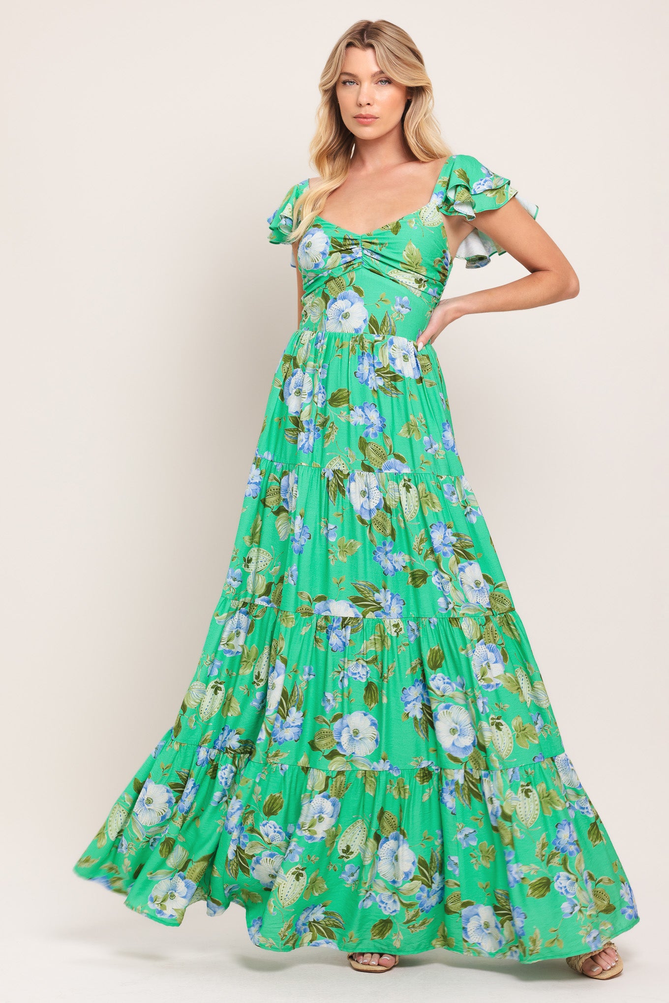 Woman wearing a green and blue floral maxi dress featuring sweetheart neckline, shirred bust, double ruffle sleeve, tier skirt and smocked back bodice | Flying Tomato