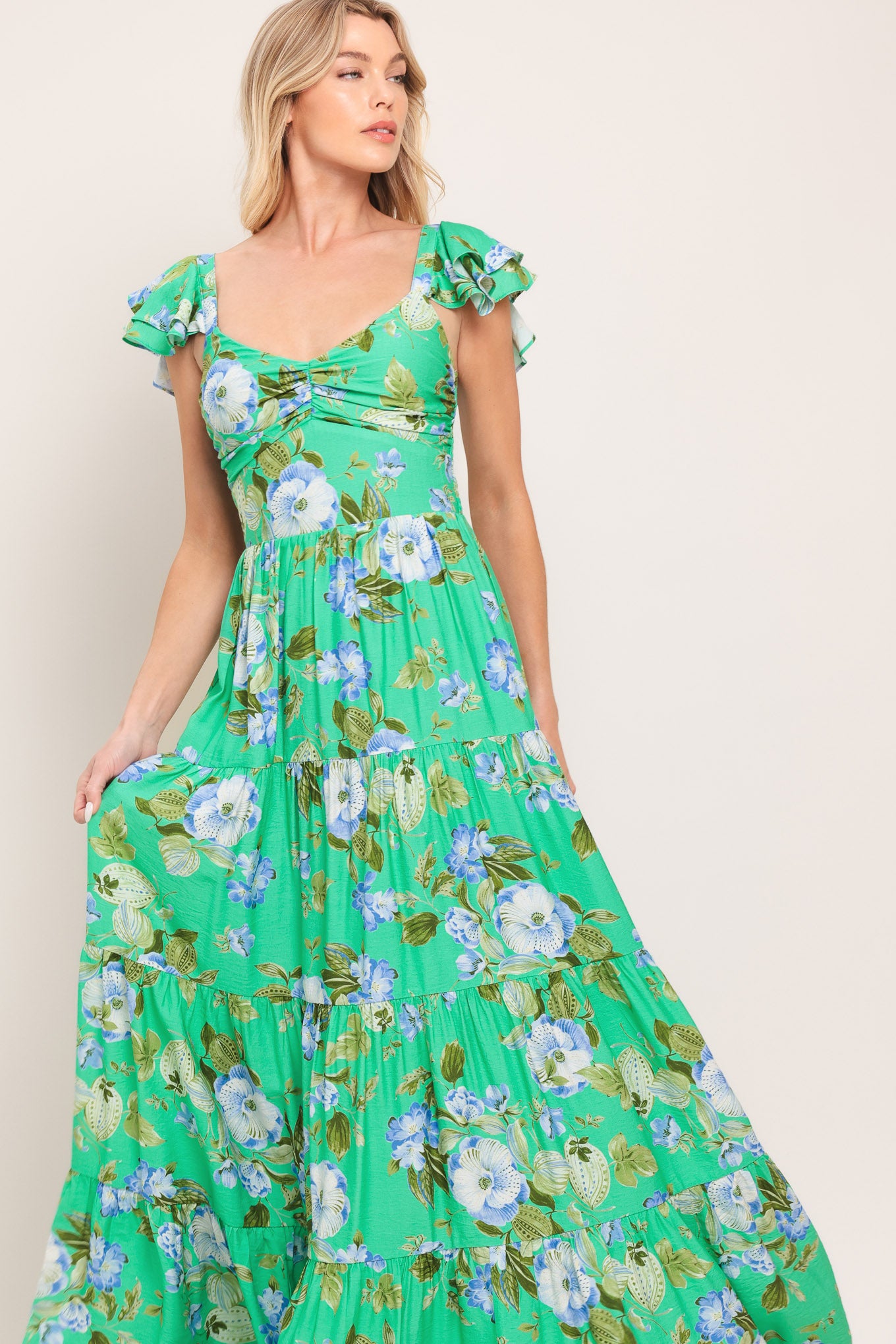 Woman wearing a green and blue floral maxi dress featuring sweetheart neckline, shirred bust, double ruffle sleeve, tier skirt and smocked back bodice | Flying Tomato