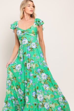 Woman wearing a green and blue floral maxi dress featuring sweetheart neckline, shirred bust, double ruffle sleeve, tier skirt and smocked back bodice | Flying Tomato