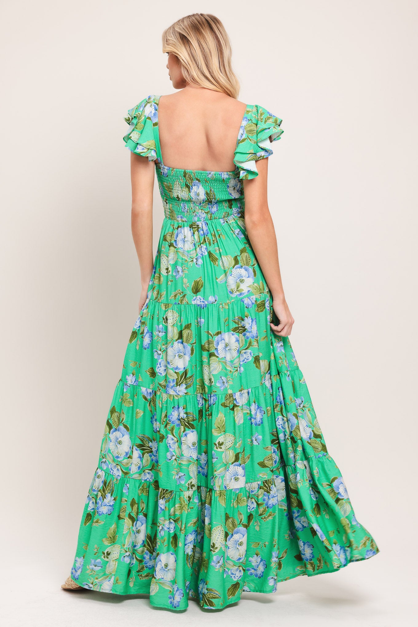 Woman wearing a green and blue floral maxi dress featuring sweetheart neckline, shirred bust, double ruffle sleeve, tier skirt and smocked back bodice | Flying Tomato