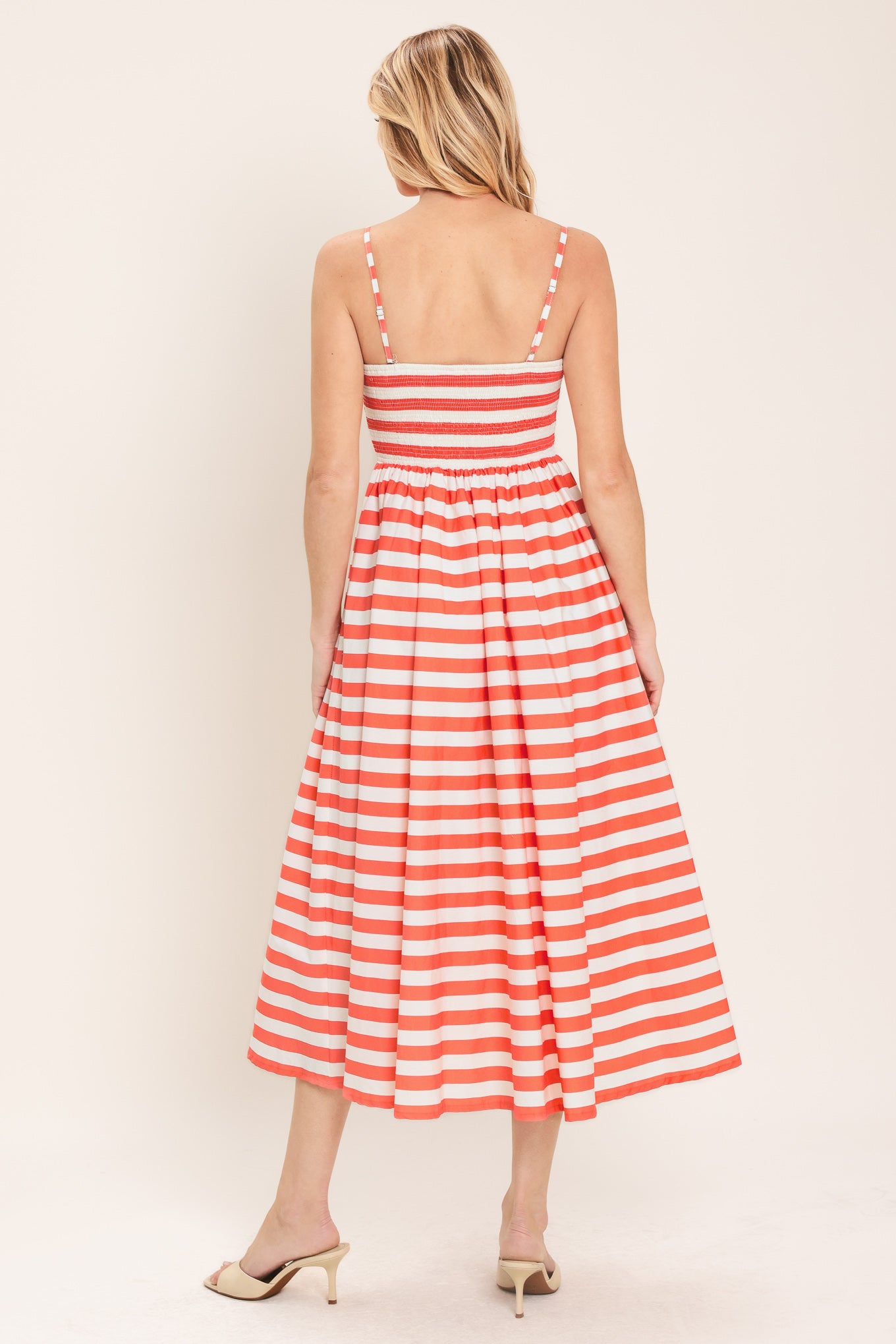 Woman wearing a coral and white striped midi dress featuring cami top, straps, full skirt and smocked back bodice | Flying Tomato