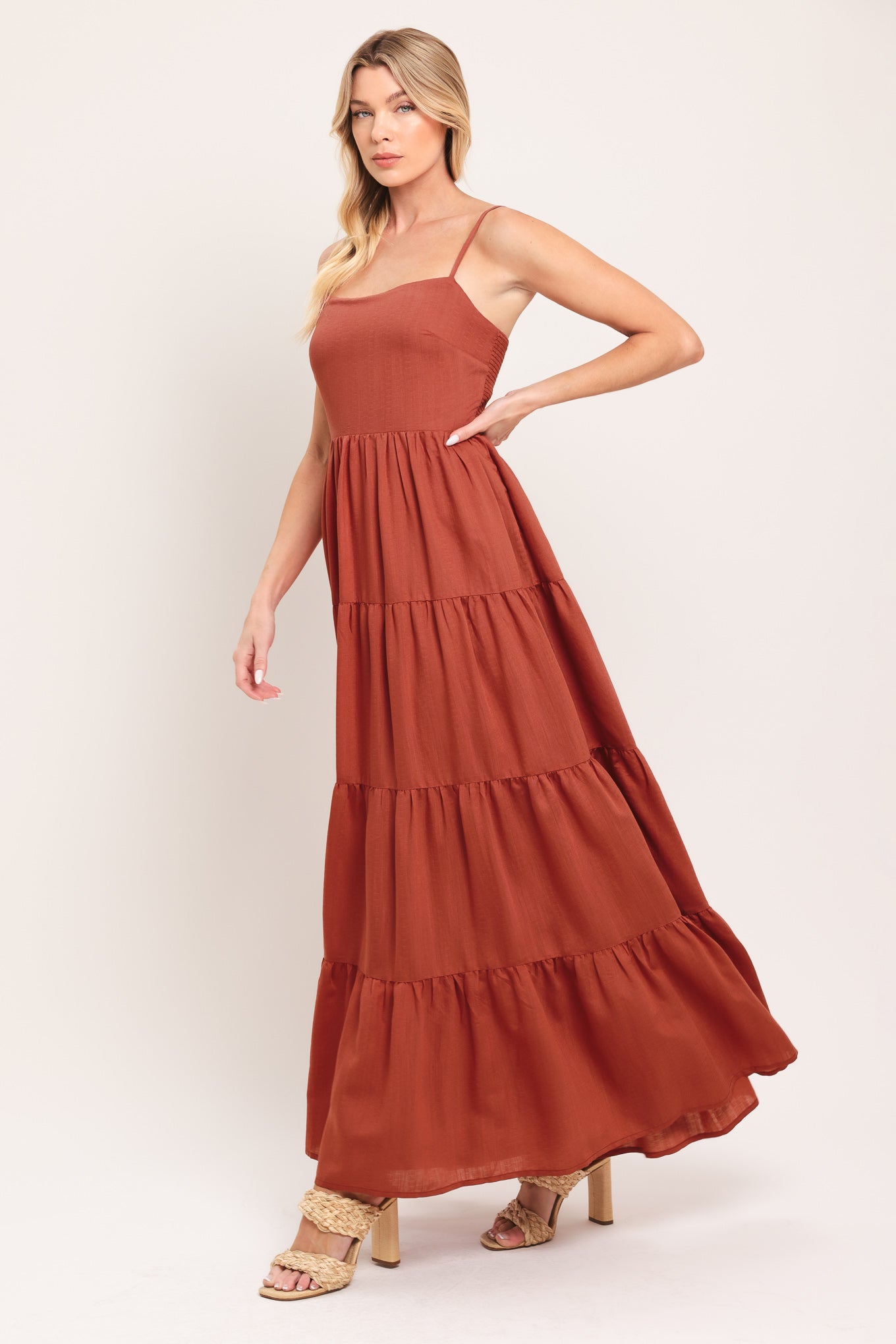 Woman wearing a rust-colored tiered maxi dress featuring cami top, tier skirt and smocked back bodice | Flying Tomato