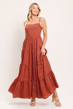 Woman wearing a rust-colored tiered maxi dress featuring cami top, tier skirt and smocked back bodice | Flying Tomato
