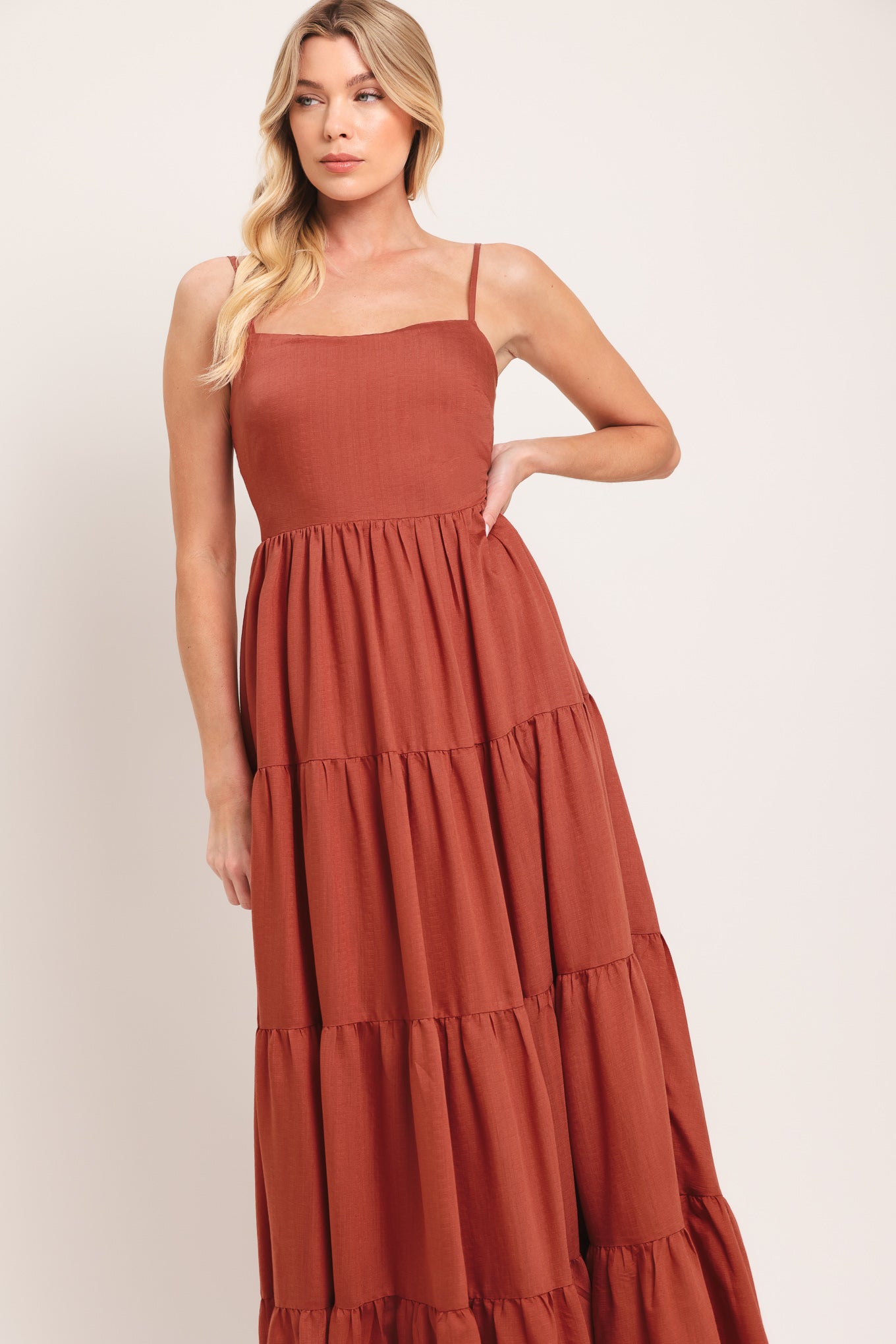 Woman wearing a rust-colored tiered maxi dress featuring cami top, tier skirt and smocked back bodice | Flying Tomato