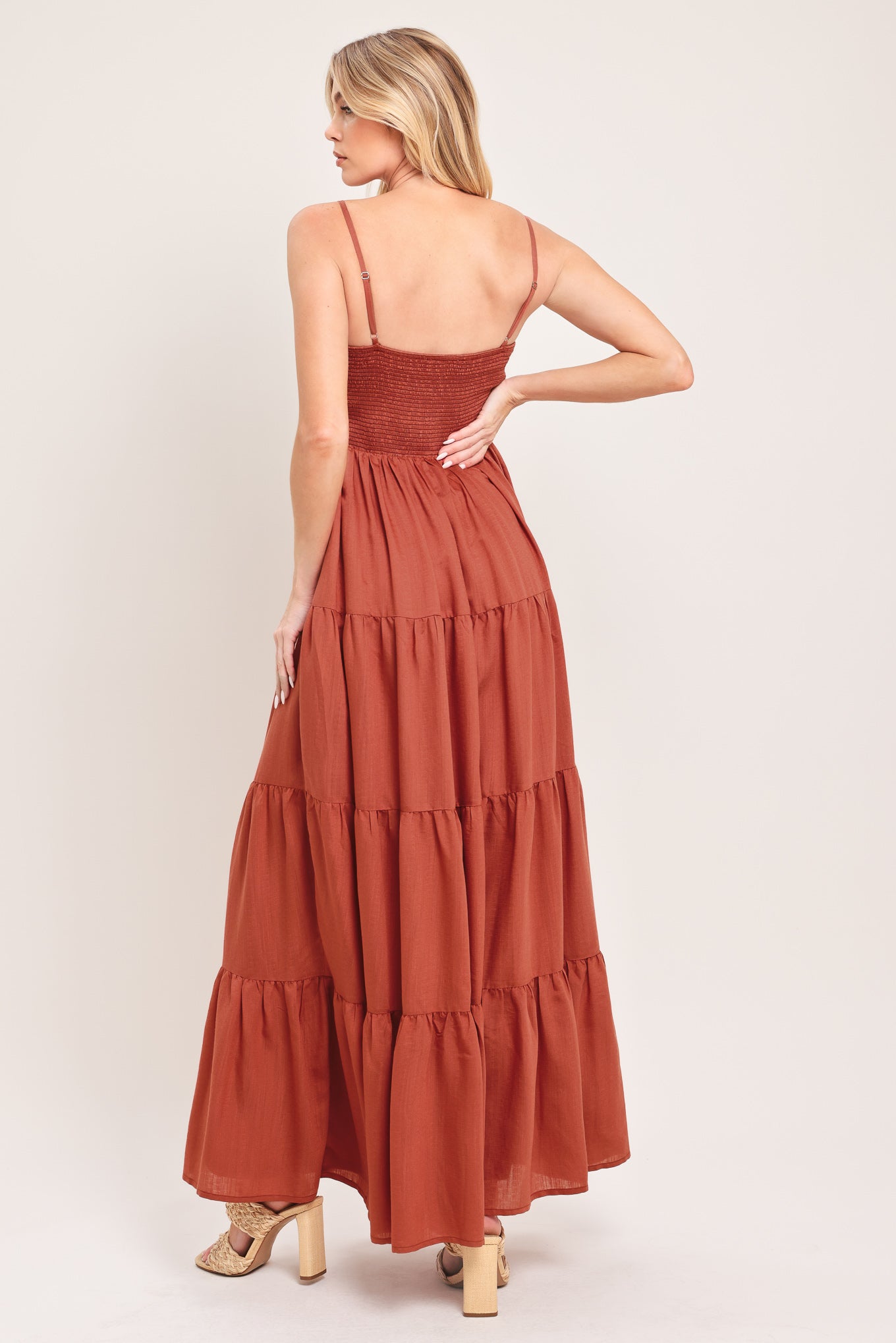 Woman wearing a rust-colored tiered maxi dress featuring cami top, tier skirt and smocked back bodice | Flying Tomato