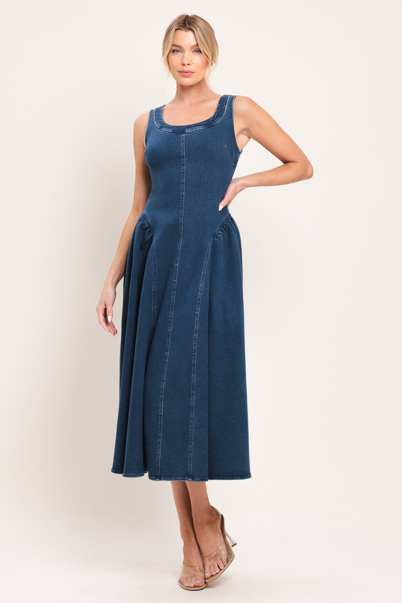 Woman wearing a sleeveless blue denim midi dress featuring U neckline, shirred side full skirt and back zipper closure | Flying Tomato