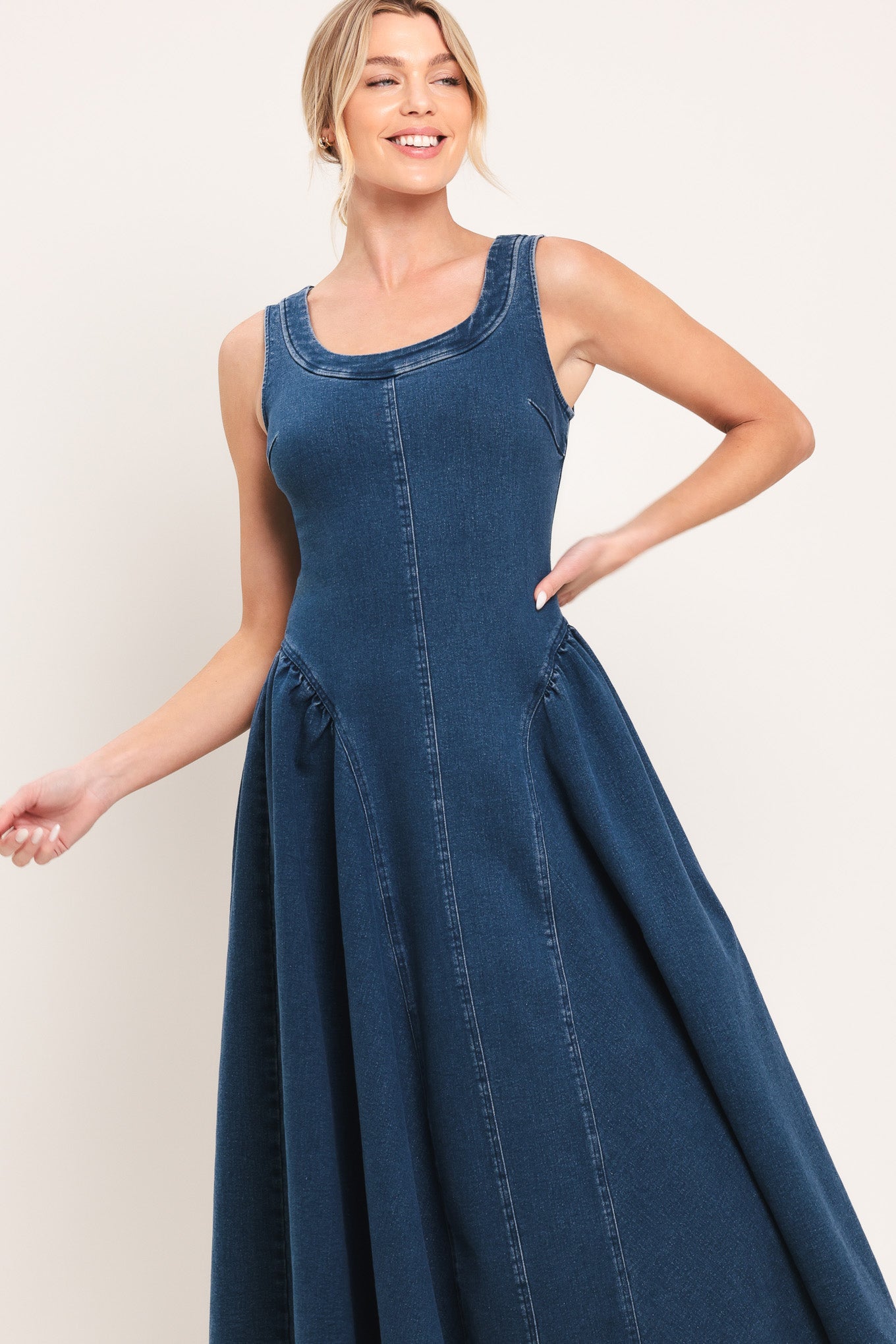 Woman wearing a sleeveless blue denim midi dress featuring U neckline, shirred side full skirt and back zipper closure | Flying Tomato